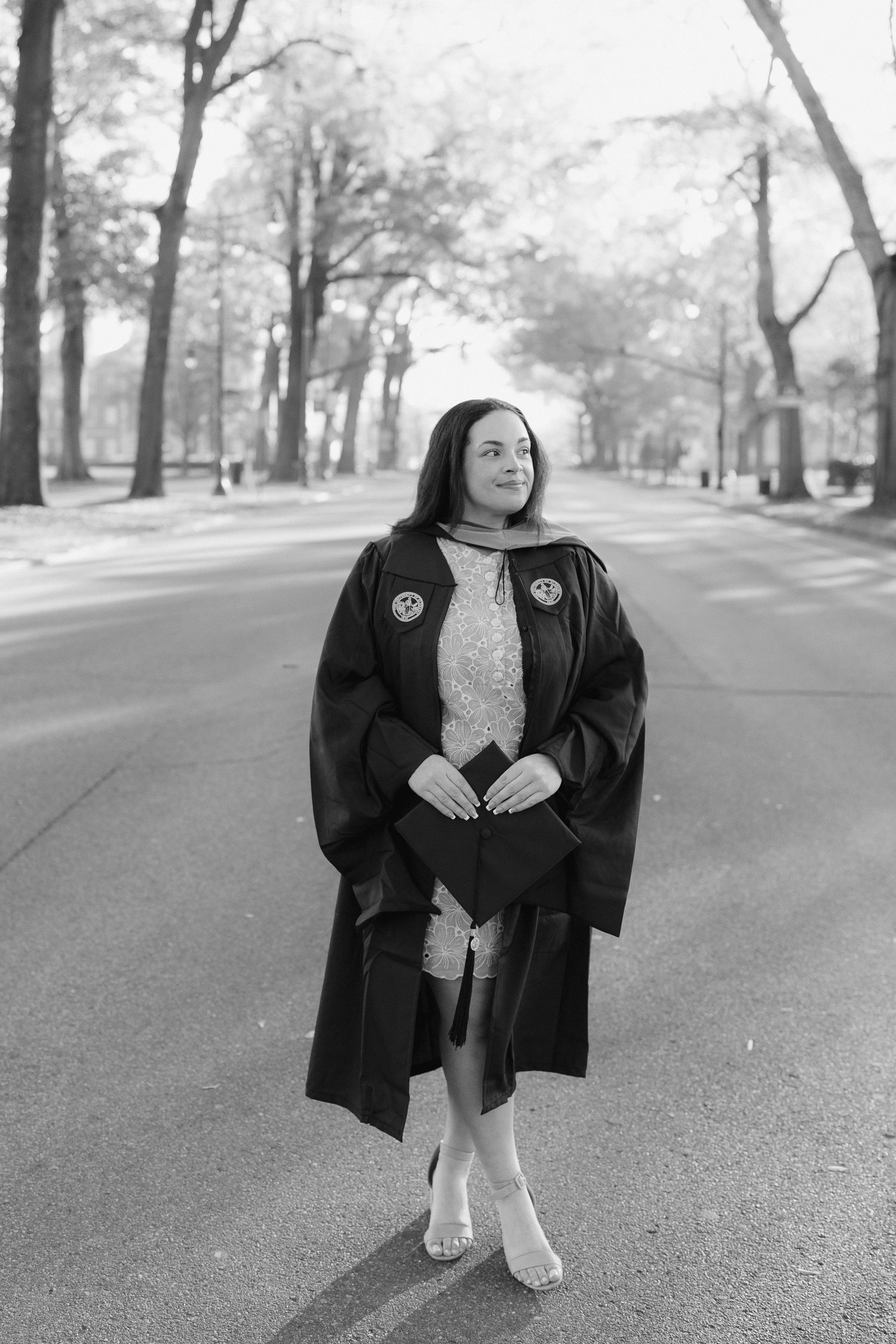 Black and white graduation portrait on tree-lined campus pathway.