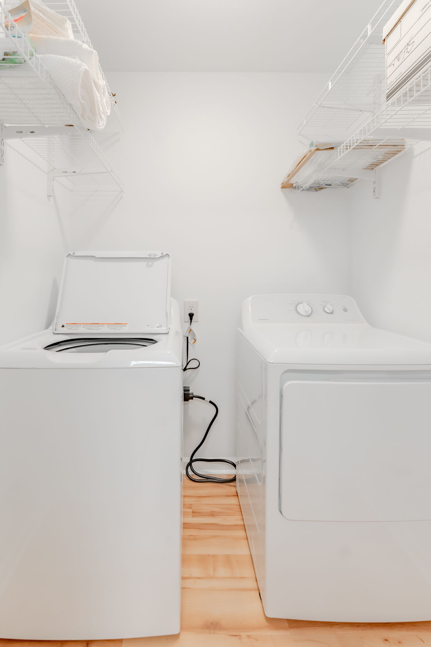 White washer and dryer appliances sit against a white wall with wooden flooring in a minimalist laundry room.