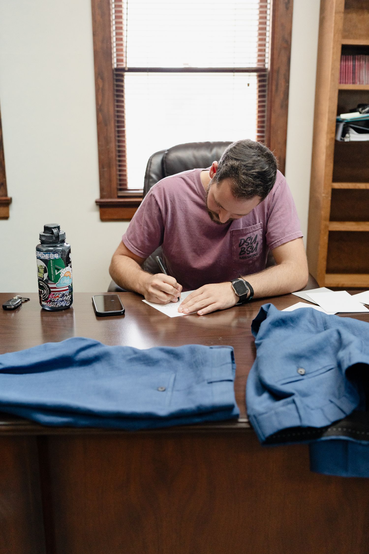 Someone writing on a navy blue fabric laid across a dark wooden desk.