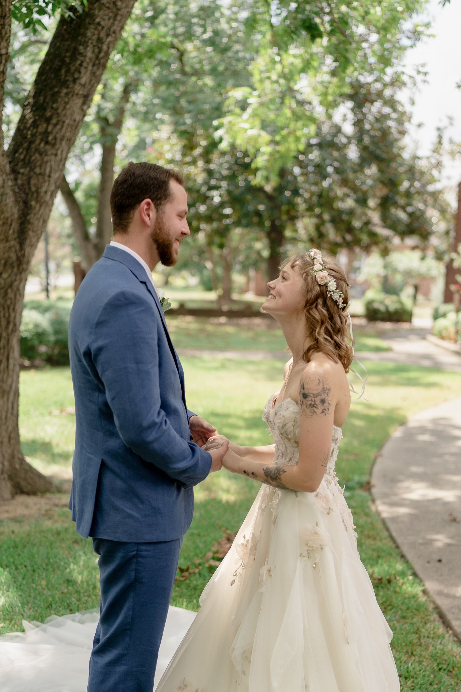 A couple in wedding attire gazes at each other lovingly in a sunlit garden setting.