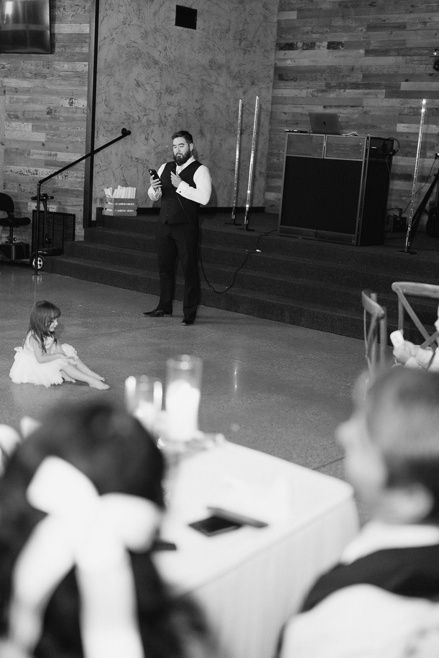Black and white photo of bearded groomsman giving speech at wedding reception.