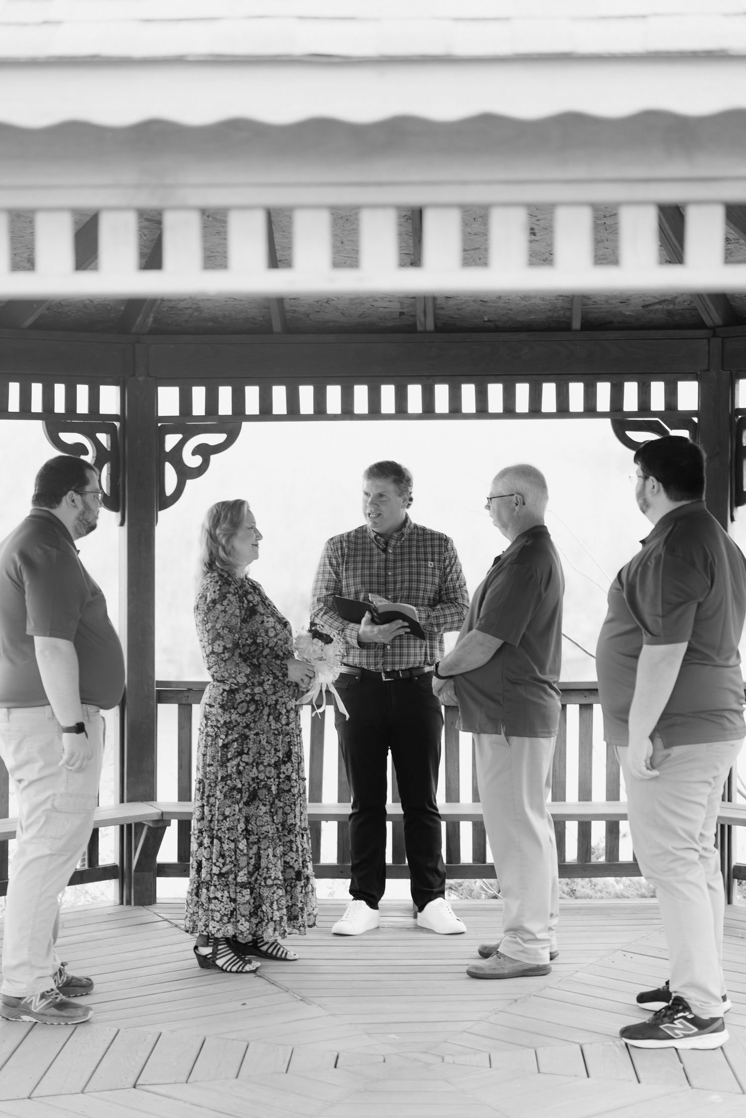 Black and white photo of a small outdoor wedding ceremony in a gazebo with five people exchanging vows.