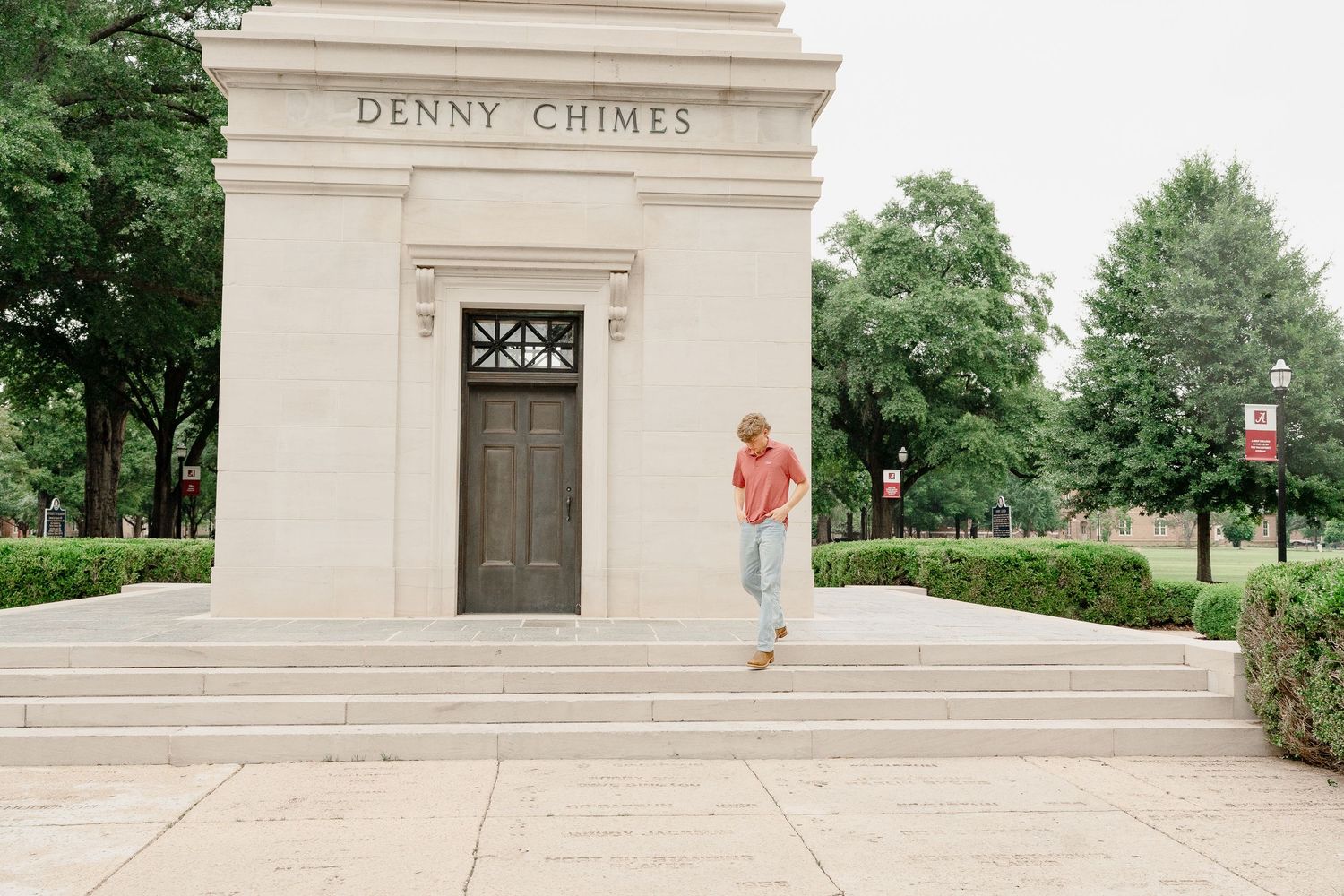 Figure in coral shirt stands casually on steps of Denny Chimes monument.