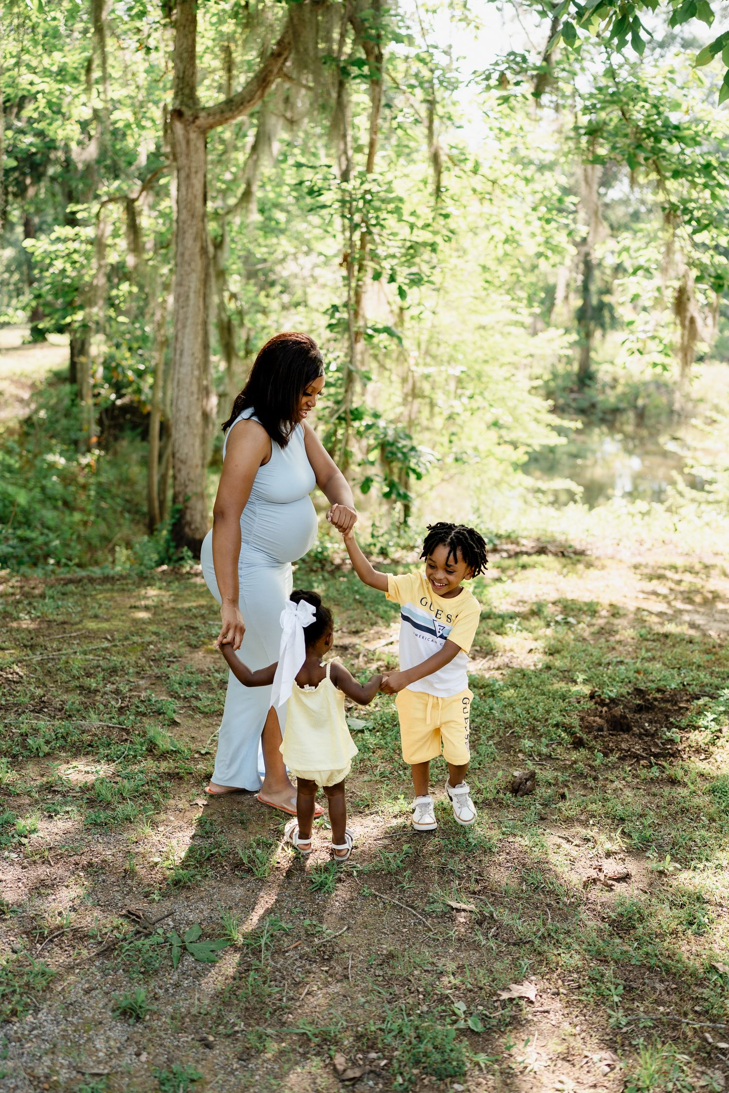 Mother and children walking and playing in dappled sunlight of wooded area.