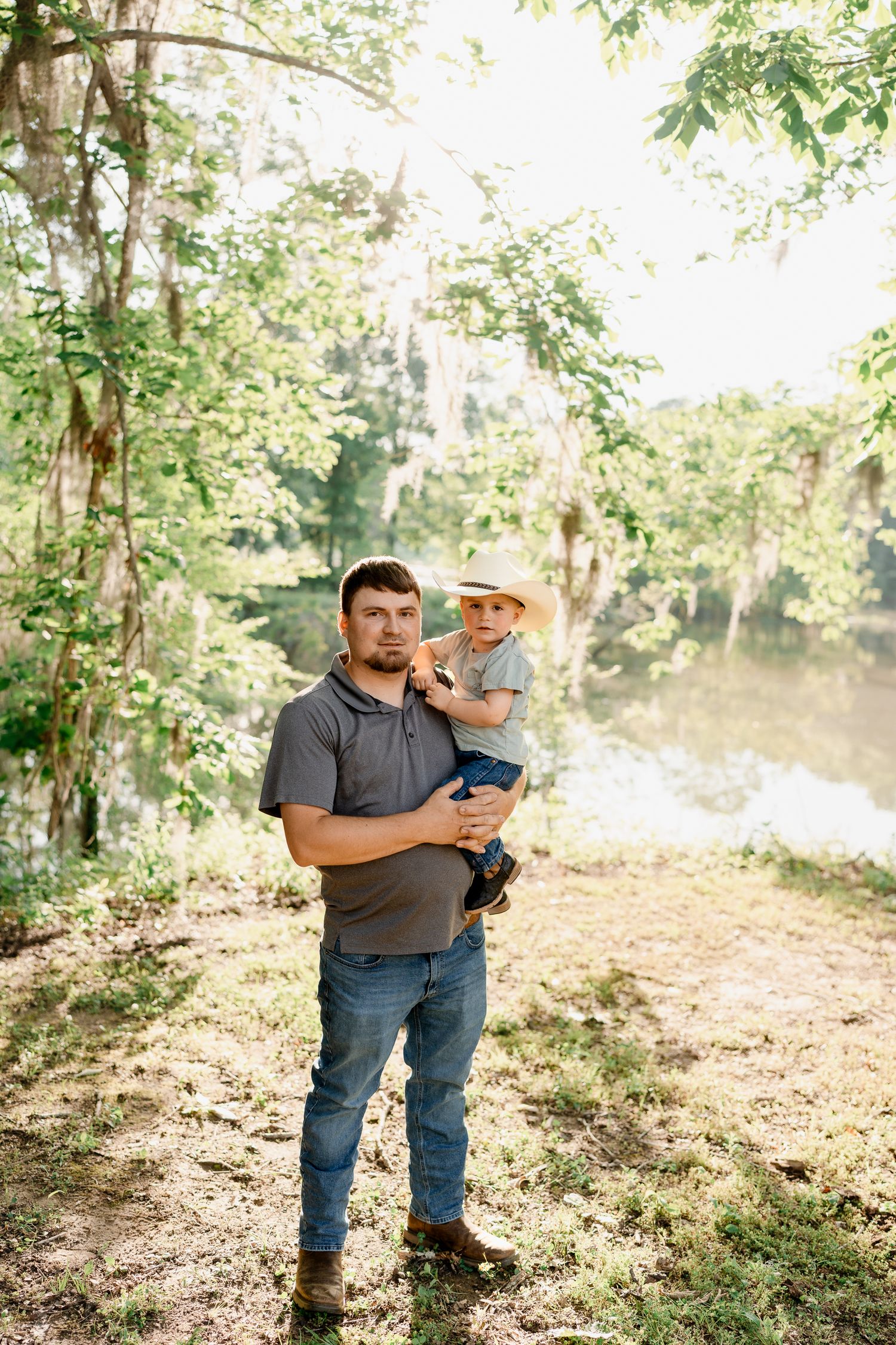Father and young child enjoy a sunny day by a pond in a wooded area.