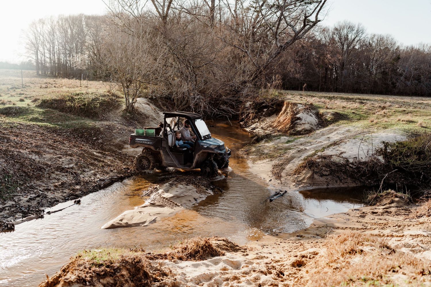 Off-road vehicle splashing through a muddy creek crossing on farm land.