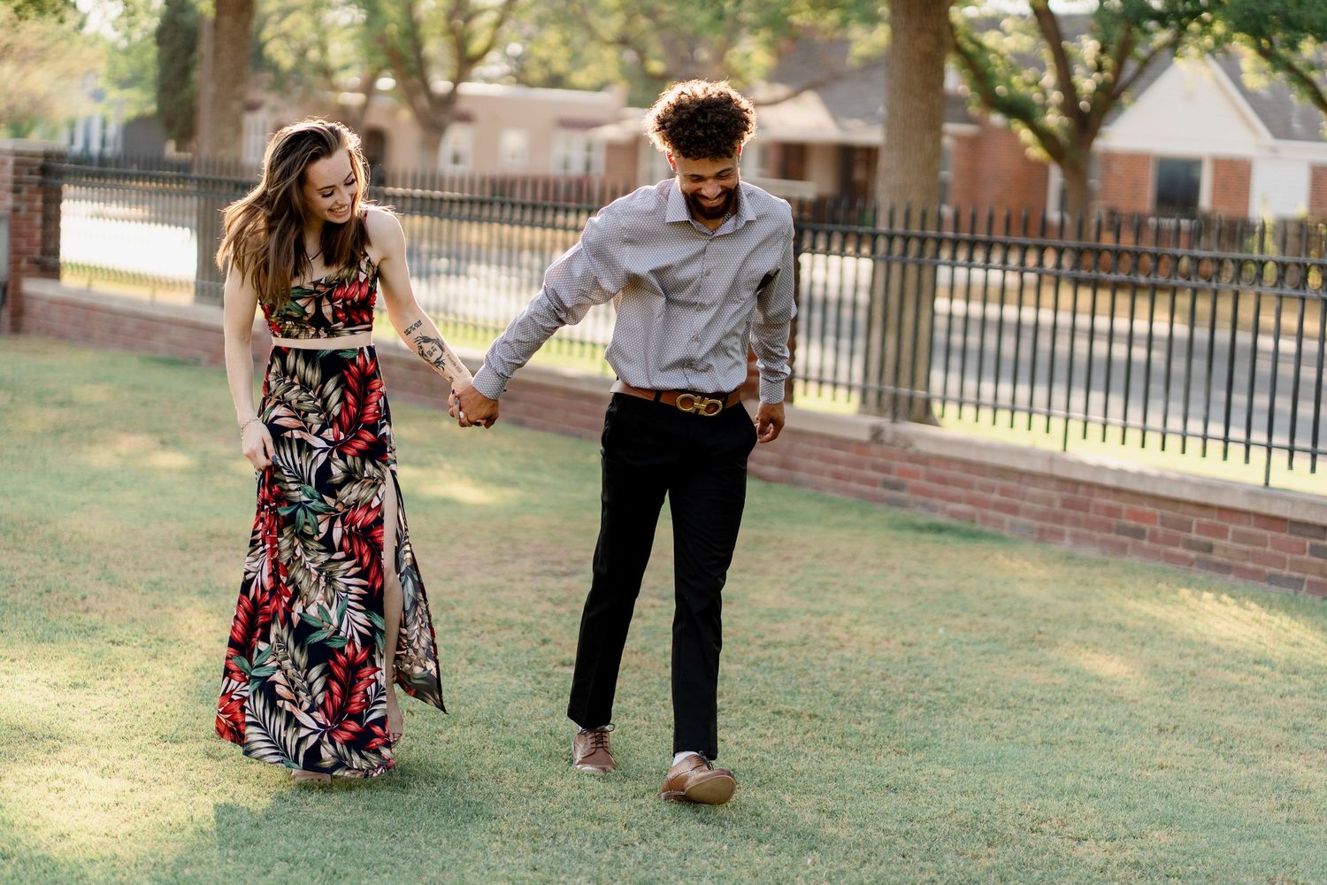 A romantic couple dances together on grass during sunset with trees in background.