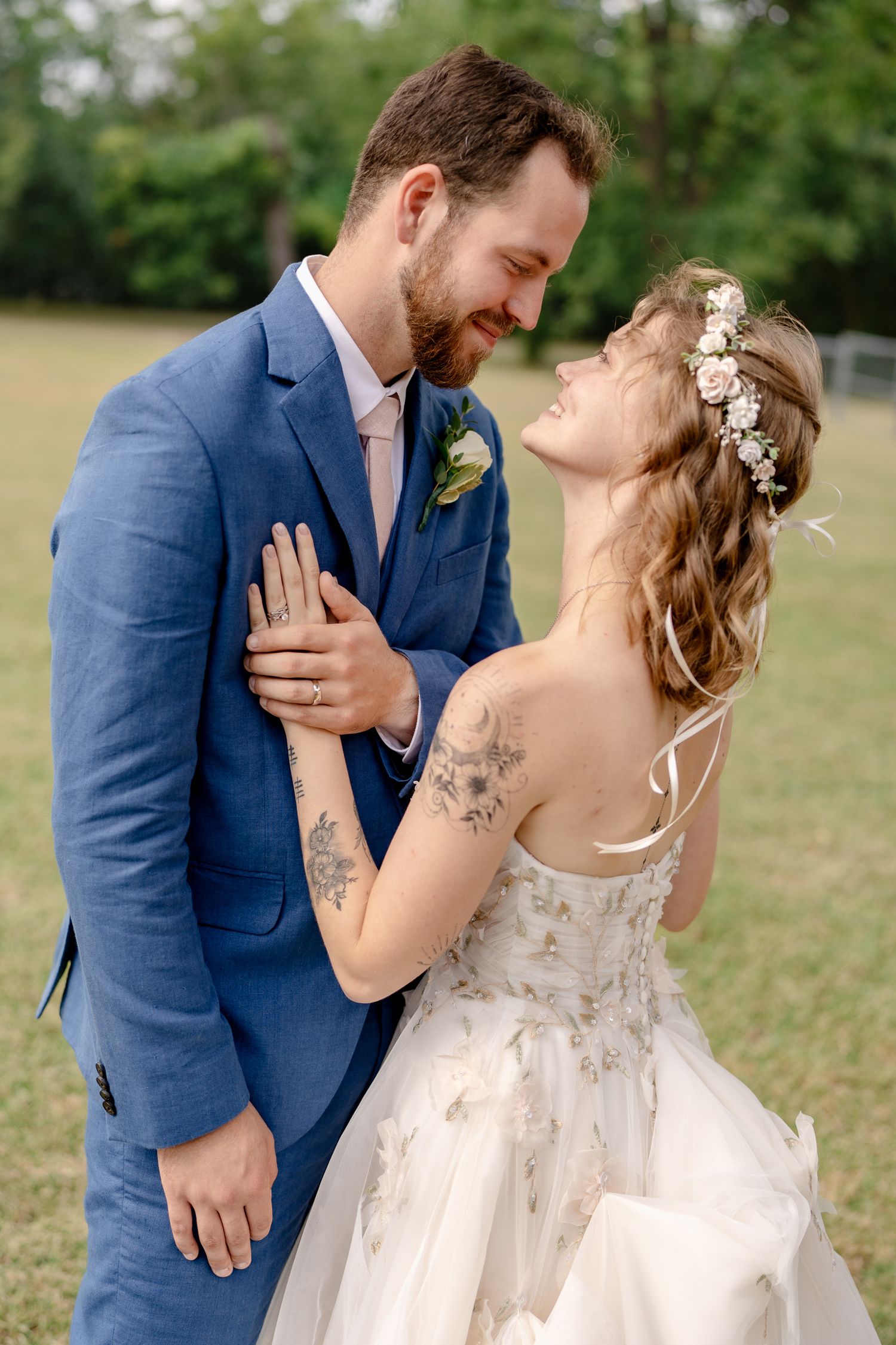 A romantic wedding couple shares intimate moments in a field while wearing blue suit and white lace dress.