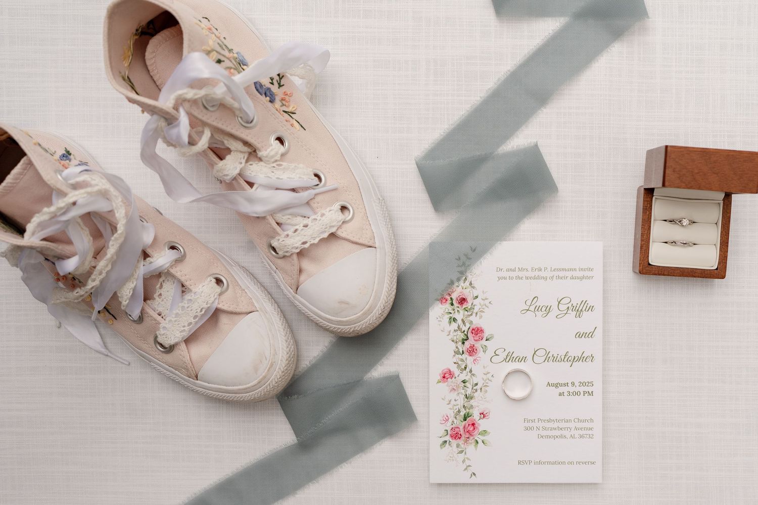Delicate wedding details including white shoes, floral invitation, and soft decor elements arranged in a flat lay.