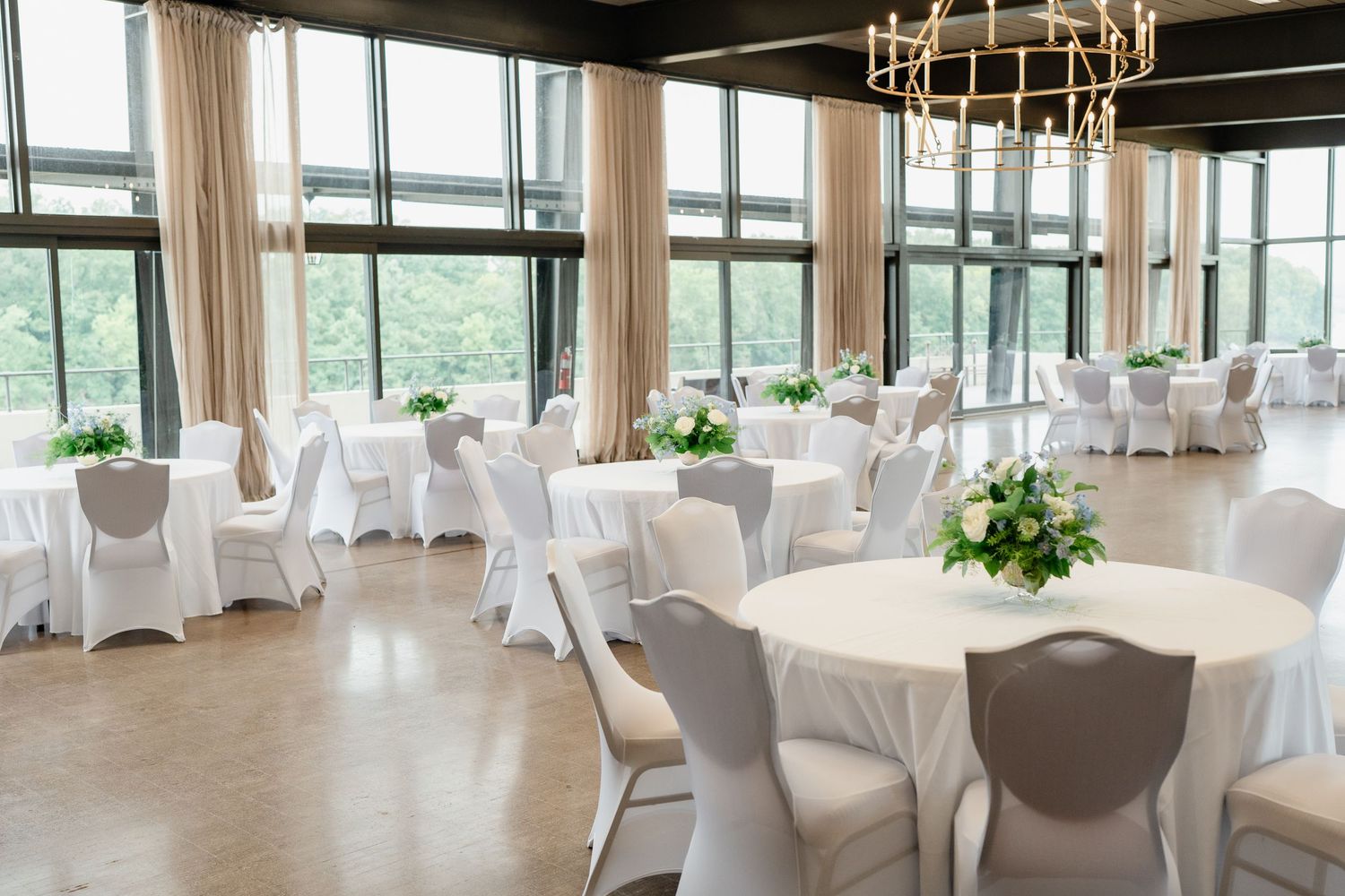 Elegant wedding reception venue with round tables, white linens, and floor-to-ceiling windows overlooking scenic views.