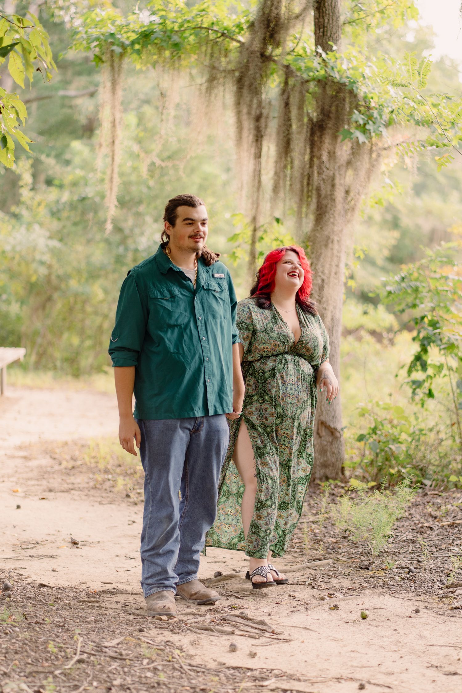 A couple shares playful and candid moments together while walking along a wooded outdoor path.