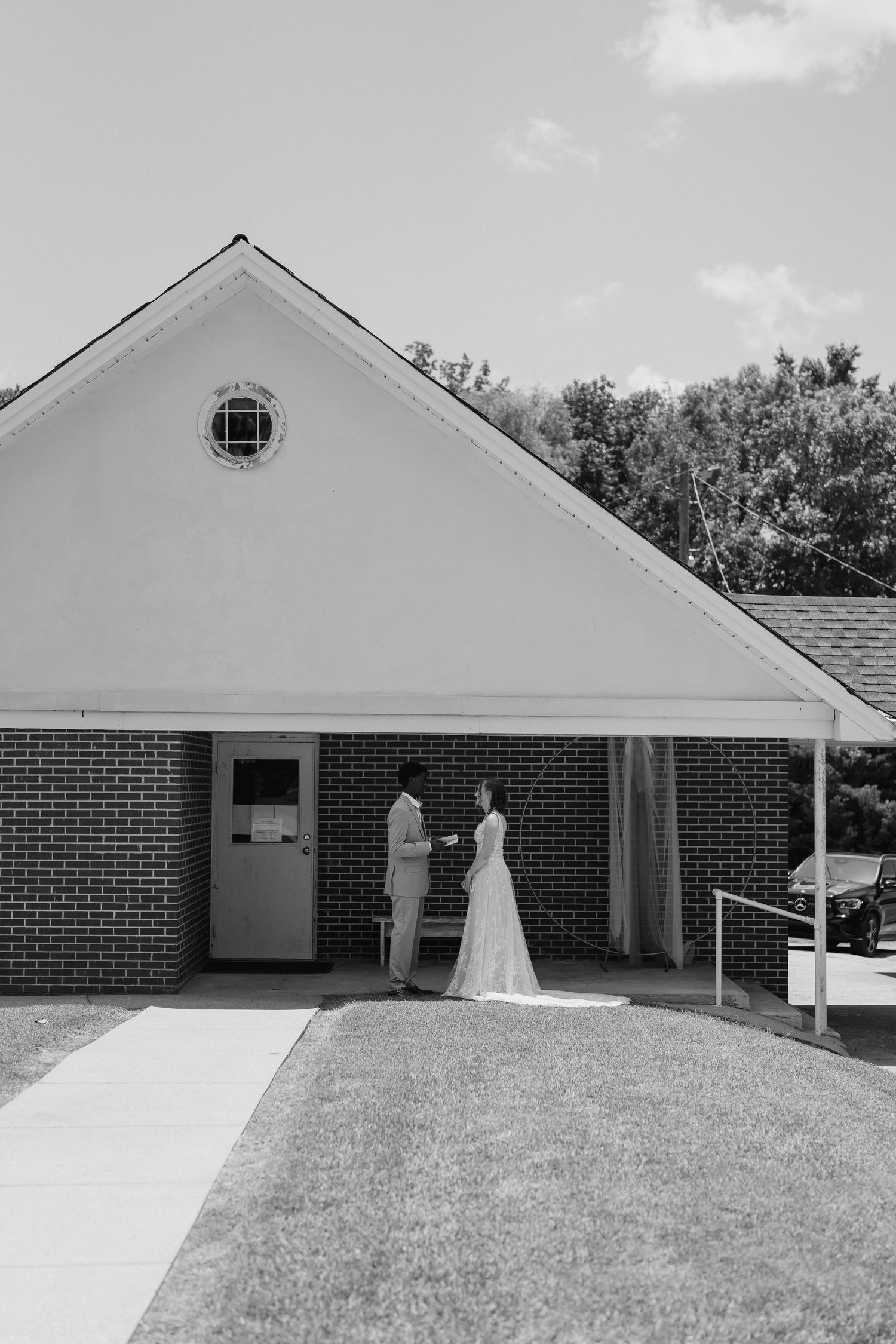 Black and white photo of bride and groom sharing a moment outside a brick church on their wedding day.