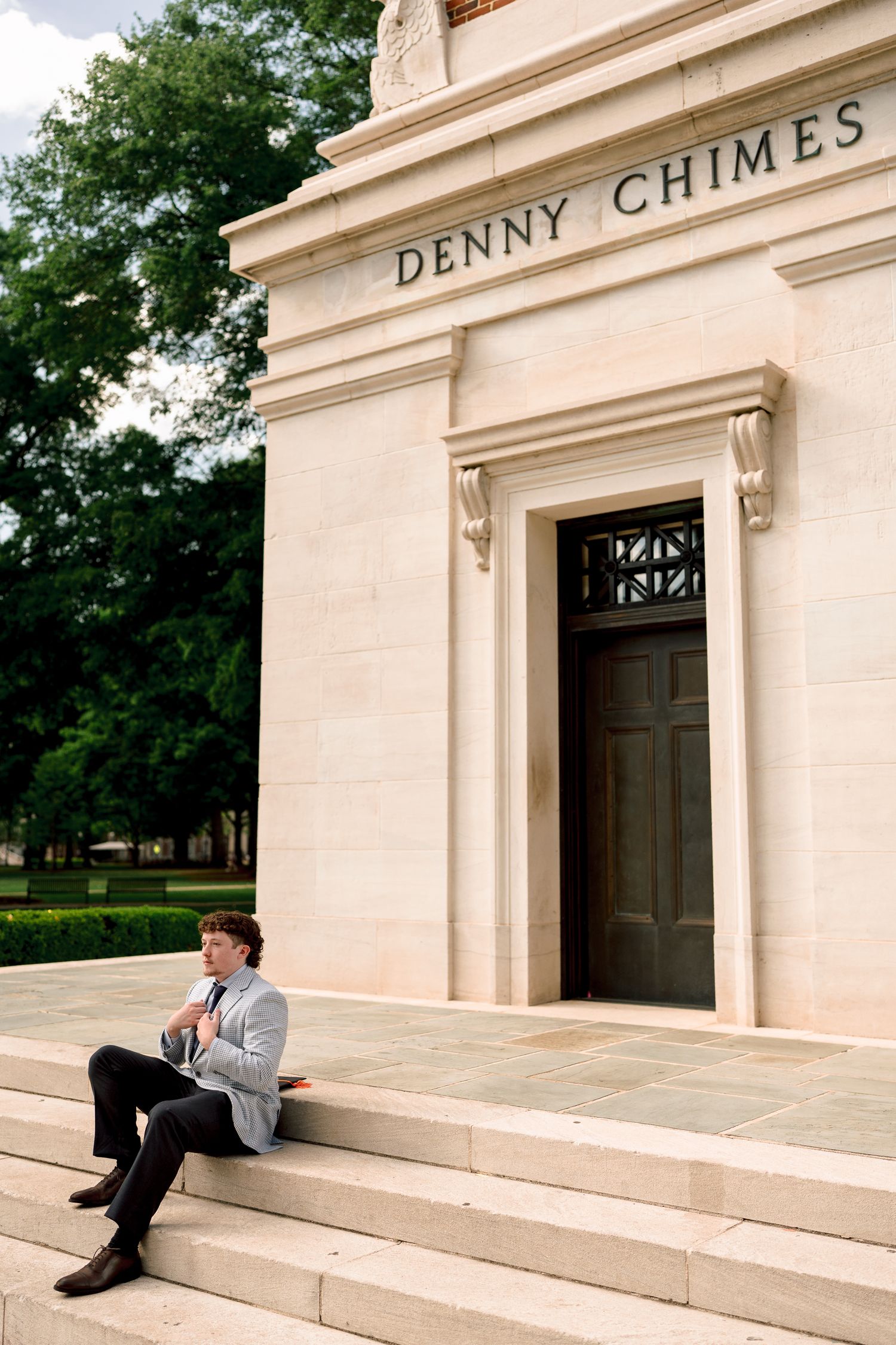 Young man in suit sitting on steps of Denny Chimes monument at University of Alabama campus.