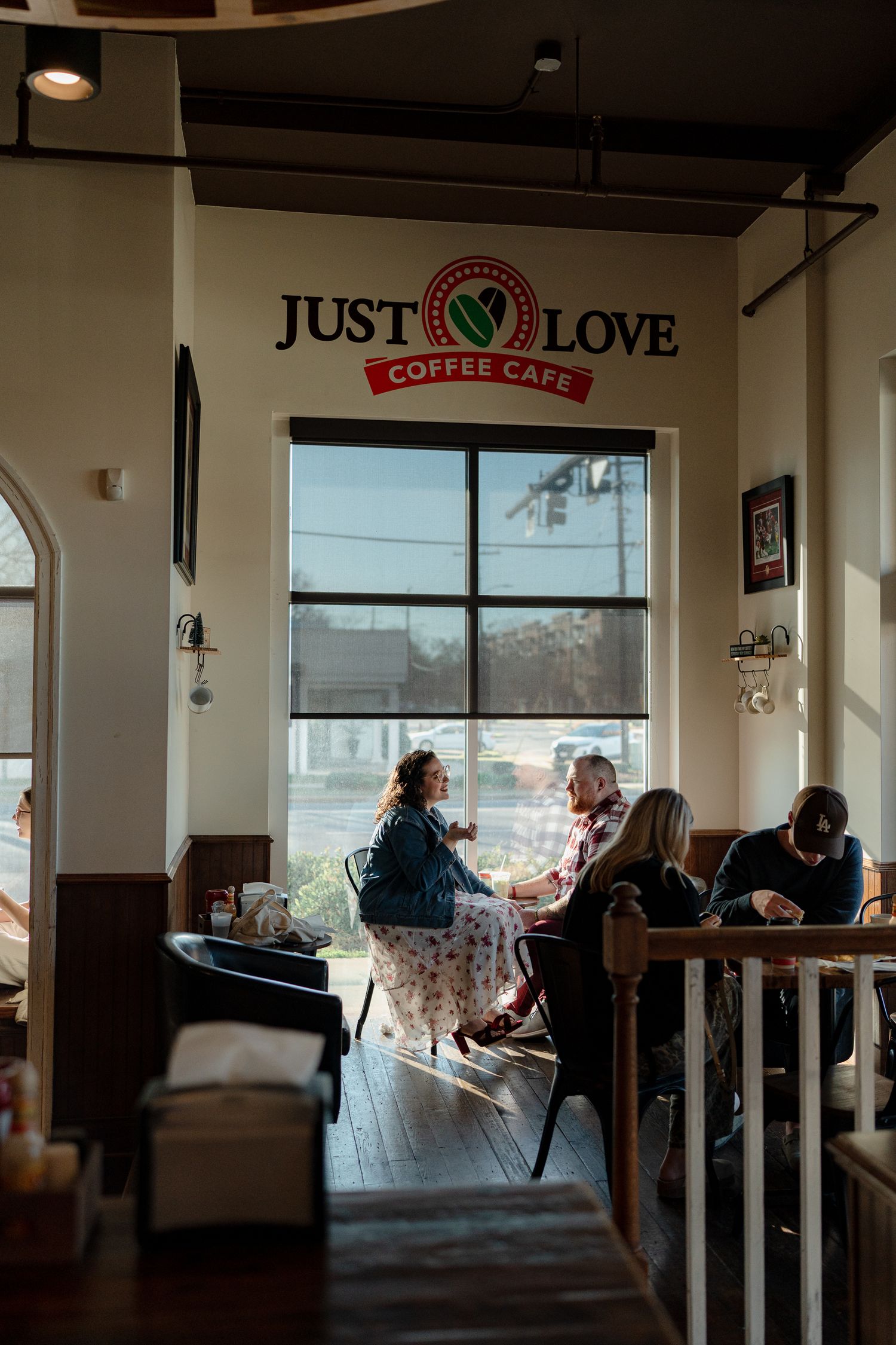 A cozy coffee shop interior with customers seated at tables near large windows on a sunny day.