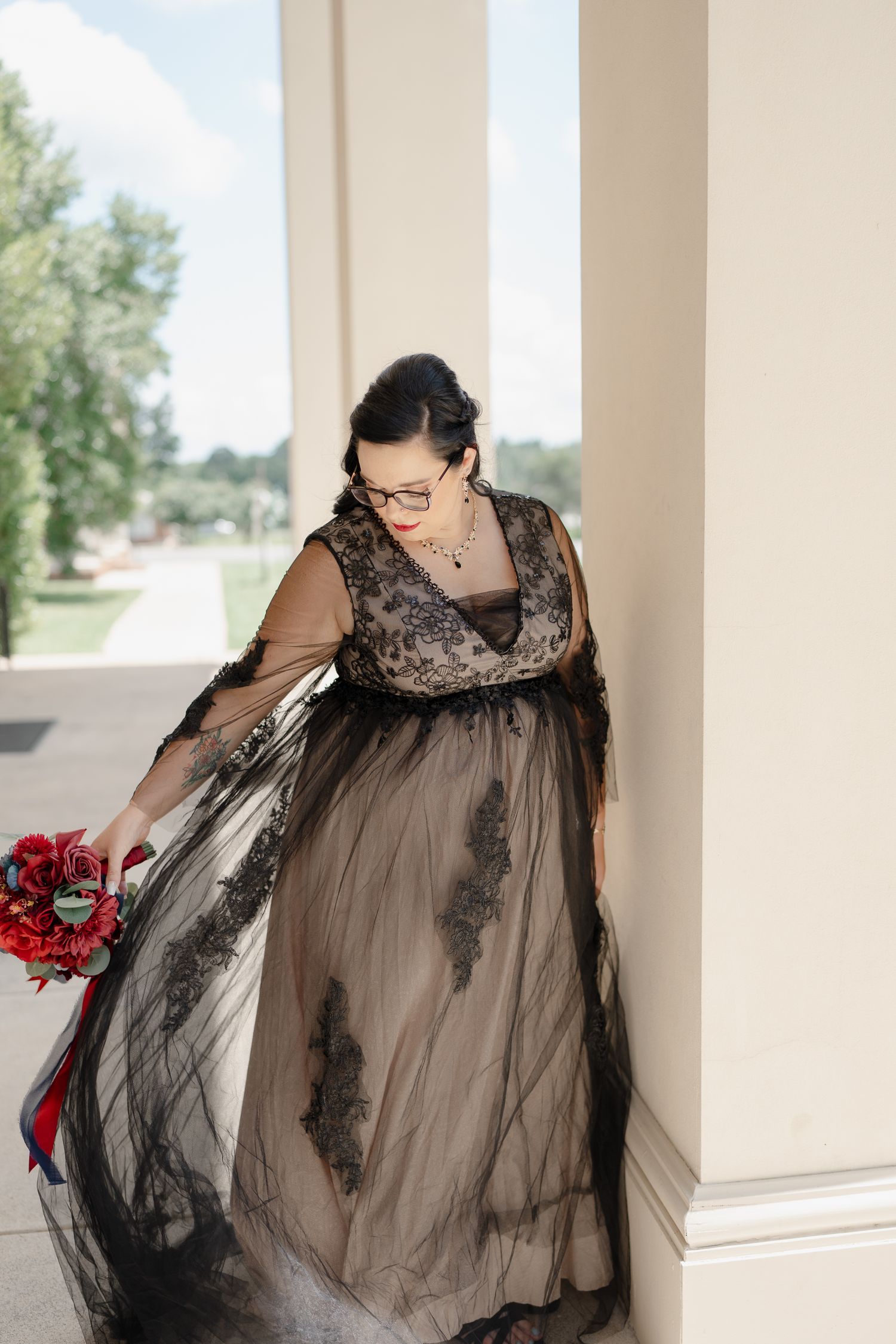 A dramatic black lace dress flows in movement against white pillars outdoors.