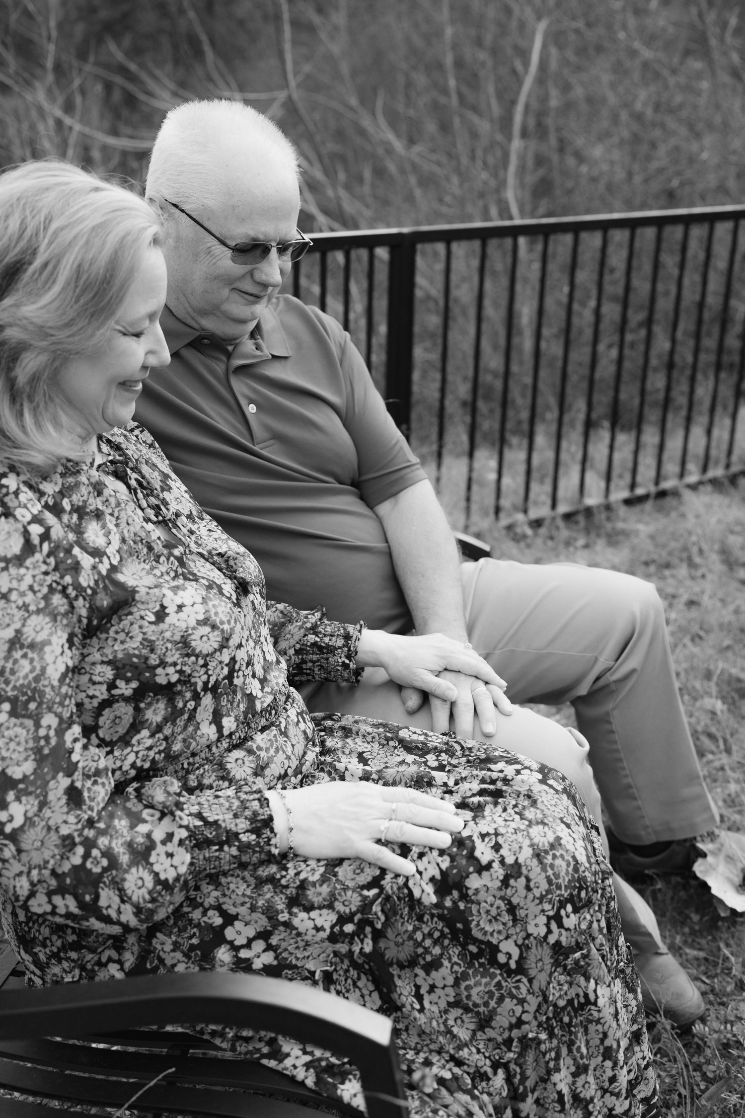 Elderly couple holding hands tenderly while seated on a bench in black and white photo.