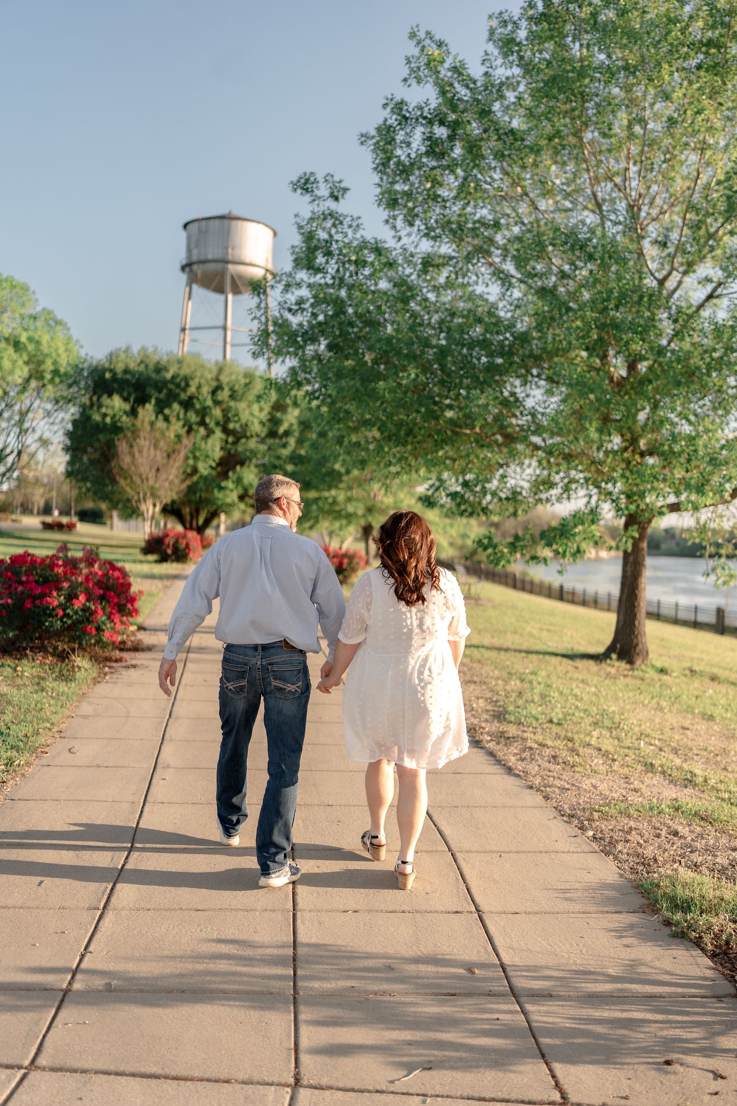 A couple strolling hand in hand on a path with a water tower in the background.