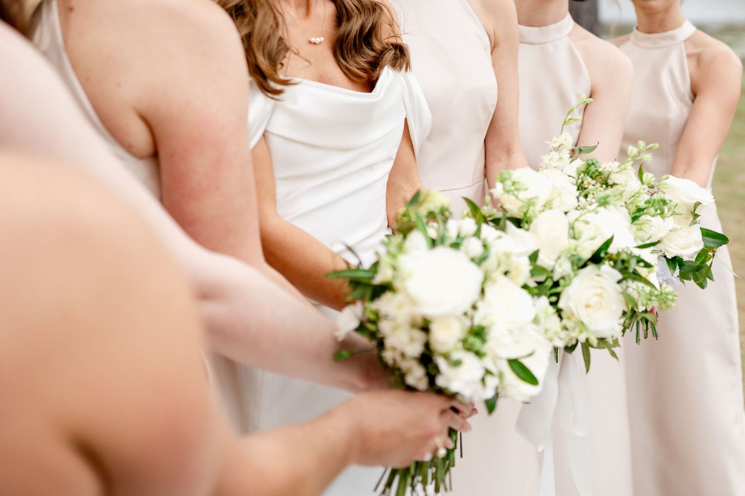 Row of bridesmaids holding elegant white and green bouquets in matching light-colored dresses.
