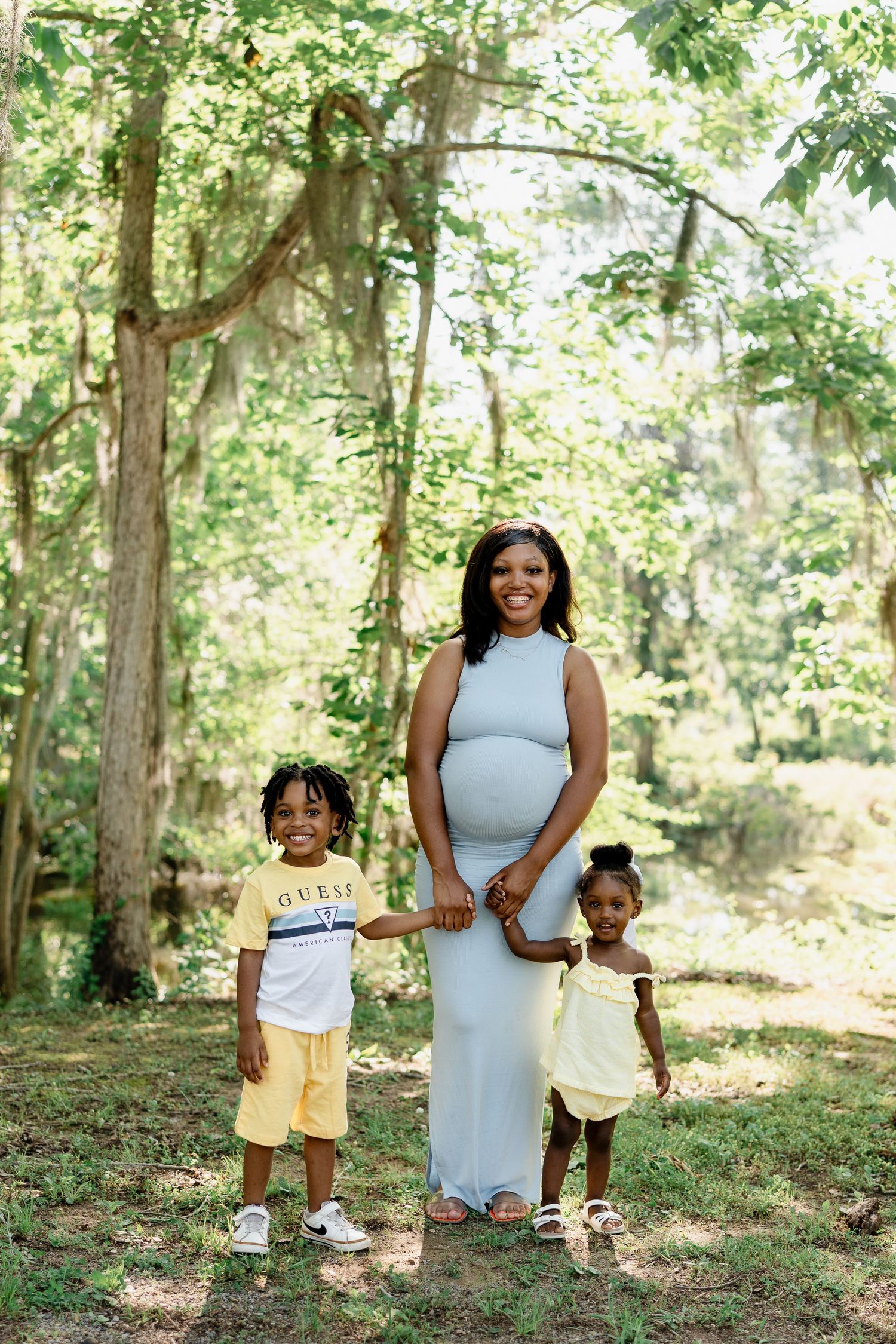 A family group poses together in a sunlit forest clearing on a warm day.
