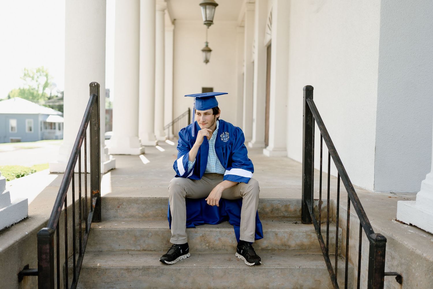 Graduate in bright blue graduation attire sits pensively between railings on stone steps.