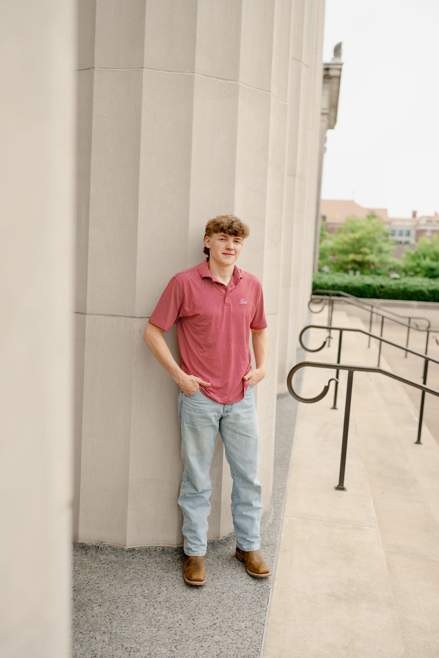 Portrait against stone column wearing striped polo shirt and jeans.