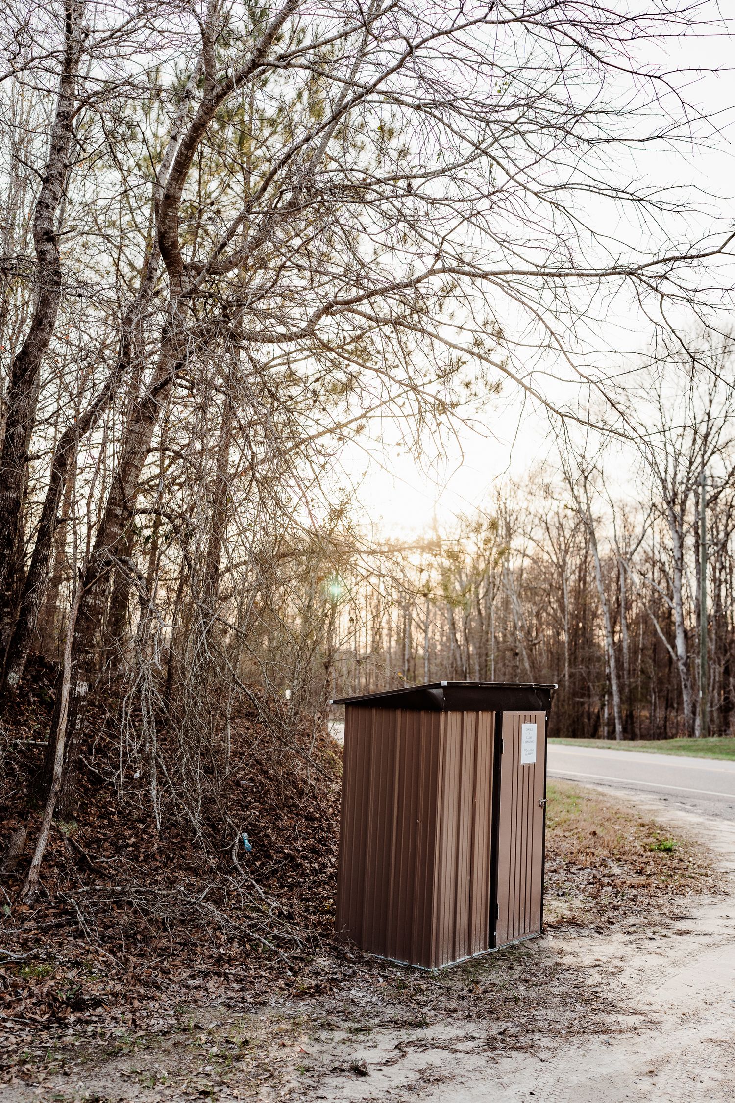 Brown metal storage unit placed along a wooded path.