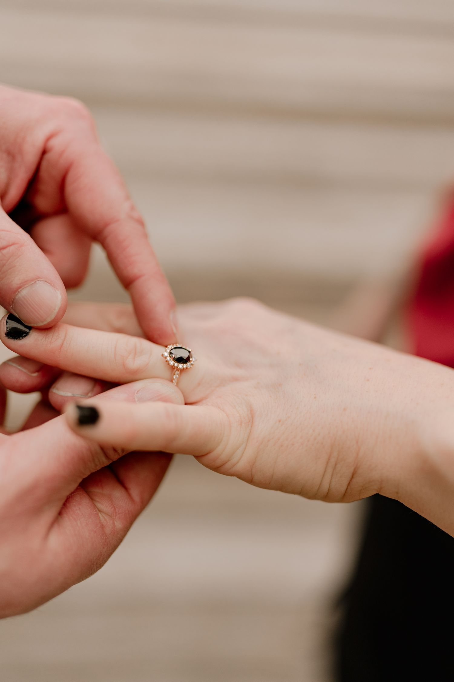 Close-up of hands placing an engagement ring with a dark gemstone on finger.