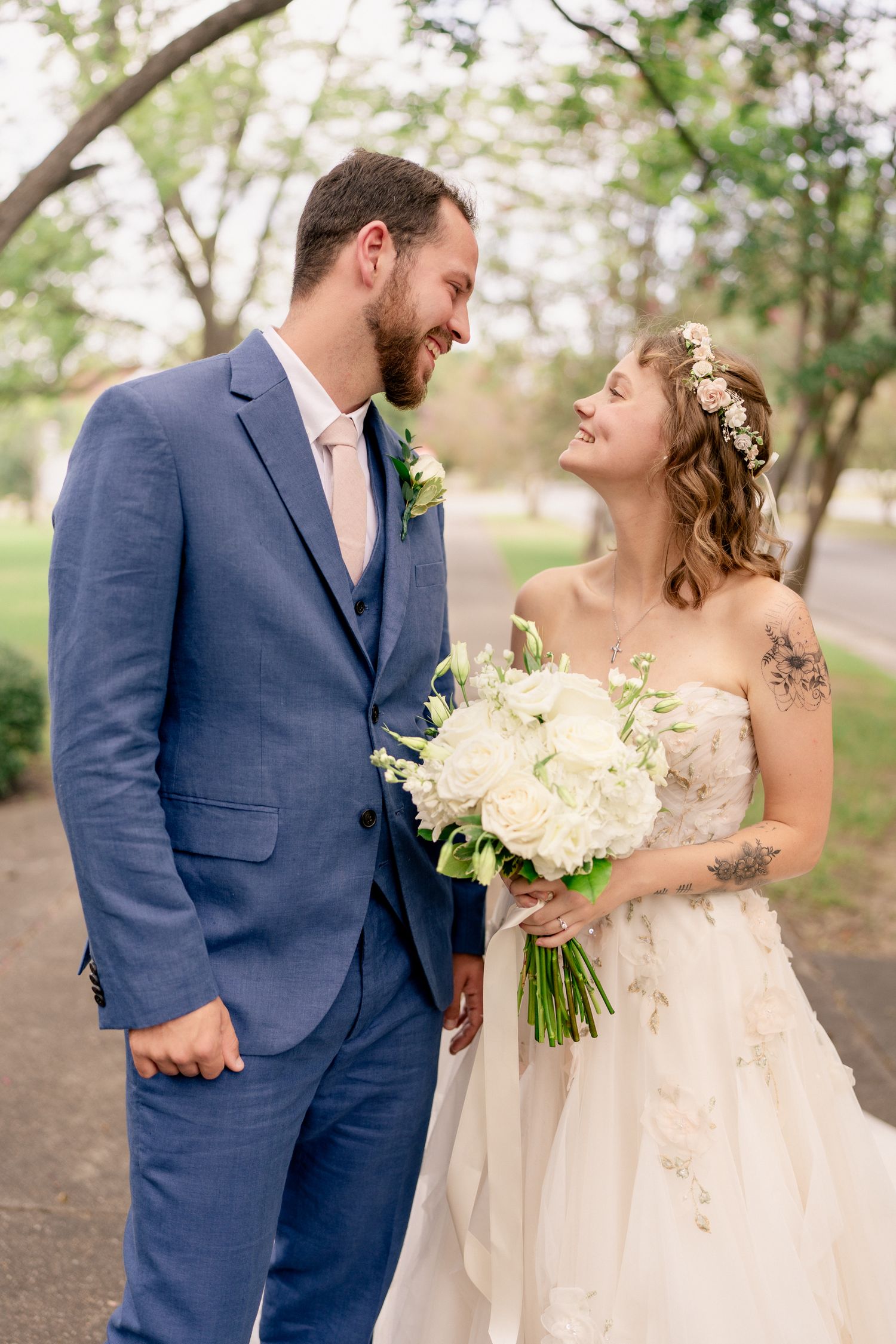 A joyful wedding couple in navy suit and cream dress share loving moments together in an outdoor garden setting.
