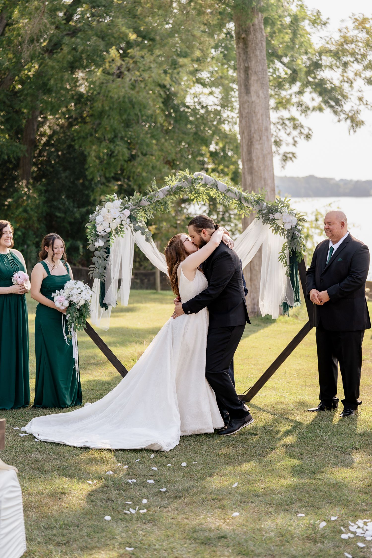 Wedding ceremony sequence showing couple and wedding party arranged around white floral arch near waterfront.