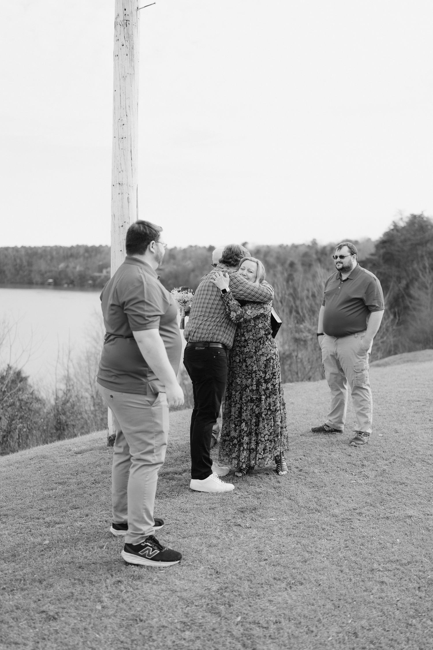 Family members embrace and celebrate after an outdoor wedding ceremony by a lake.