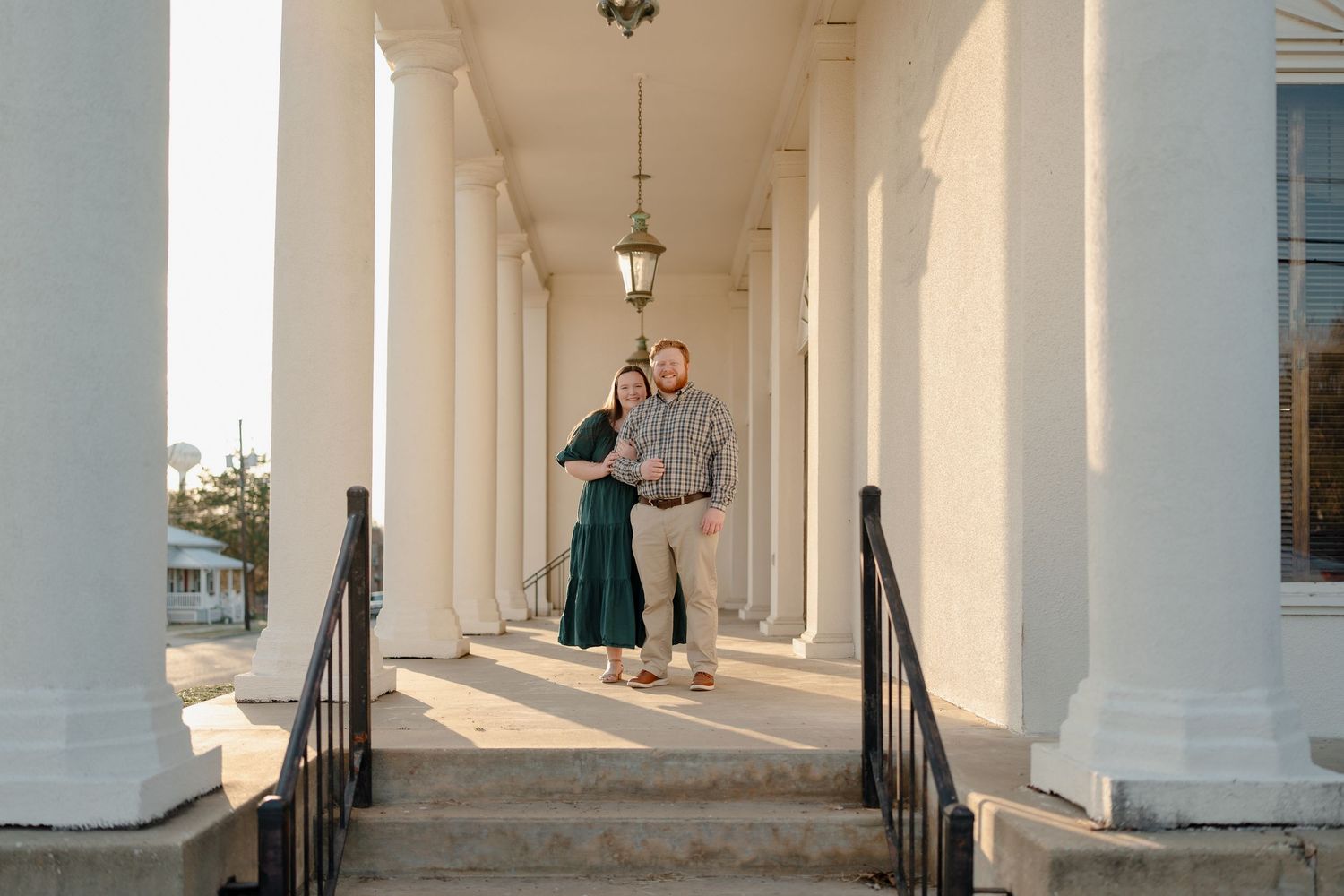 Couple standing together under white columns on grand steps of a historic building at sunset.