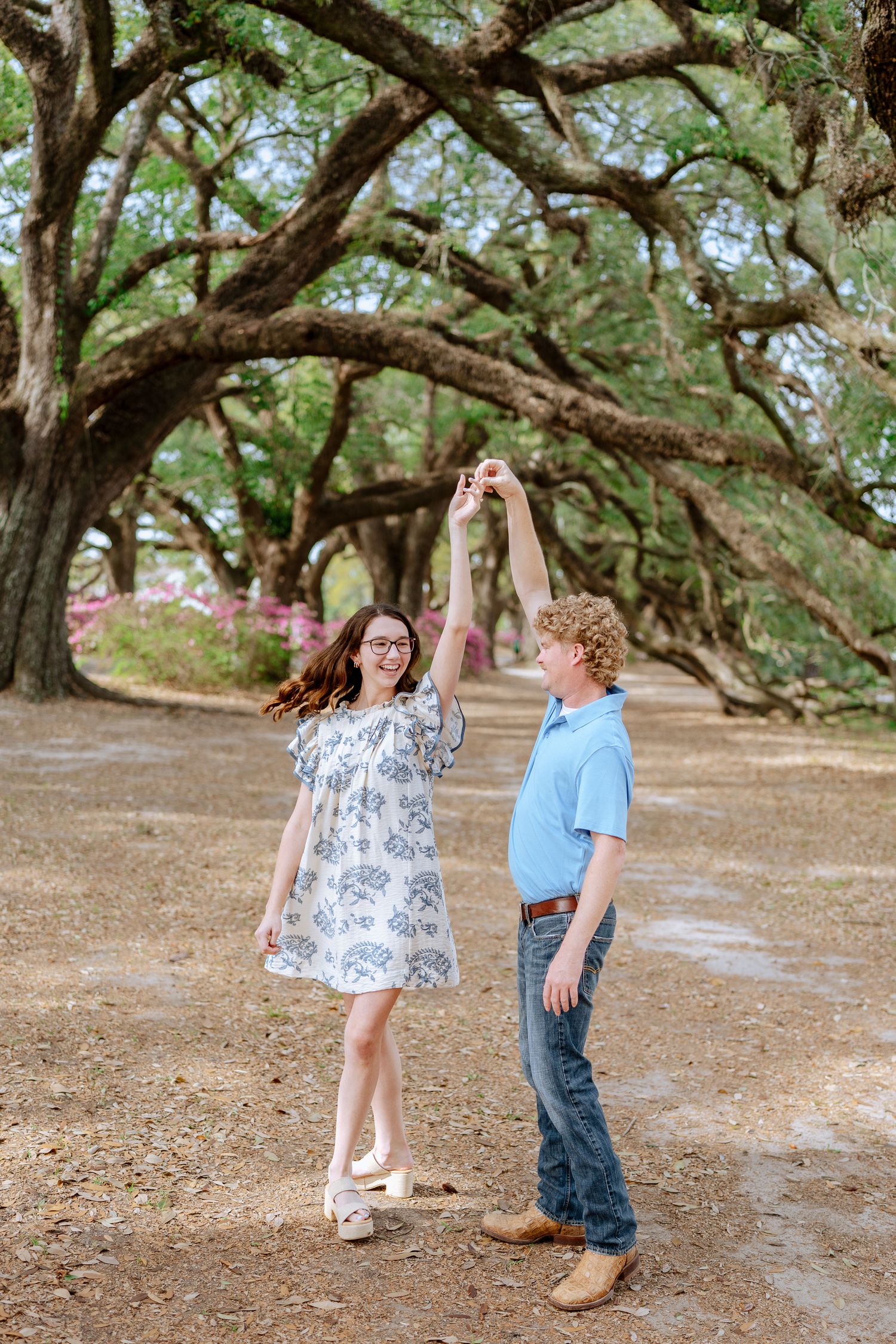 Couple in matching outfits dance playfully on tree-lined path.