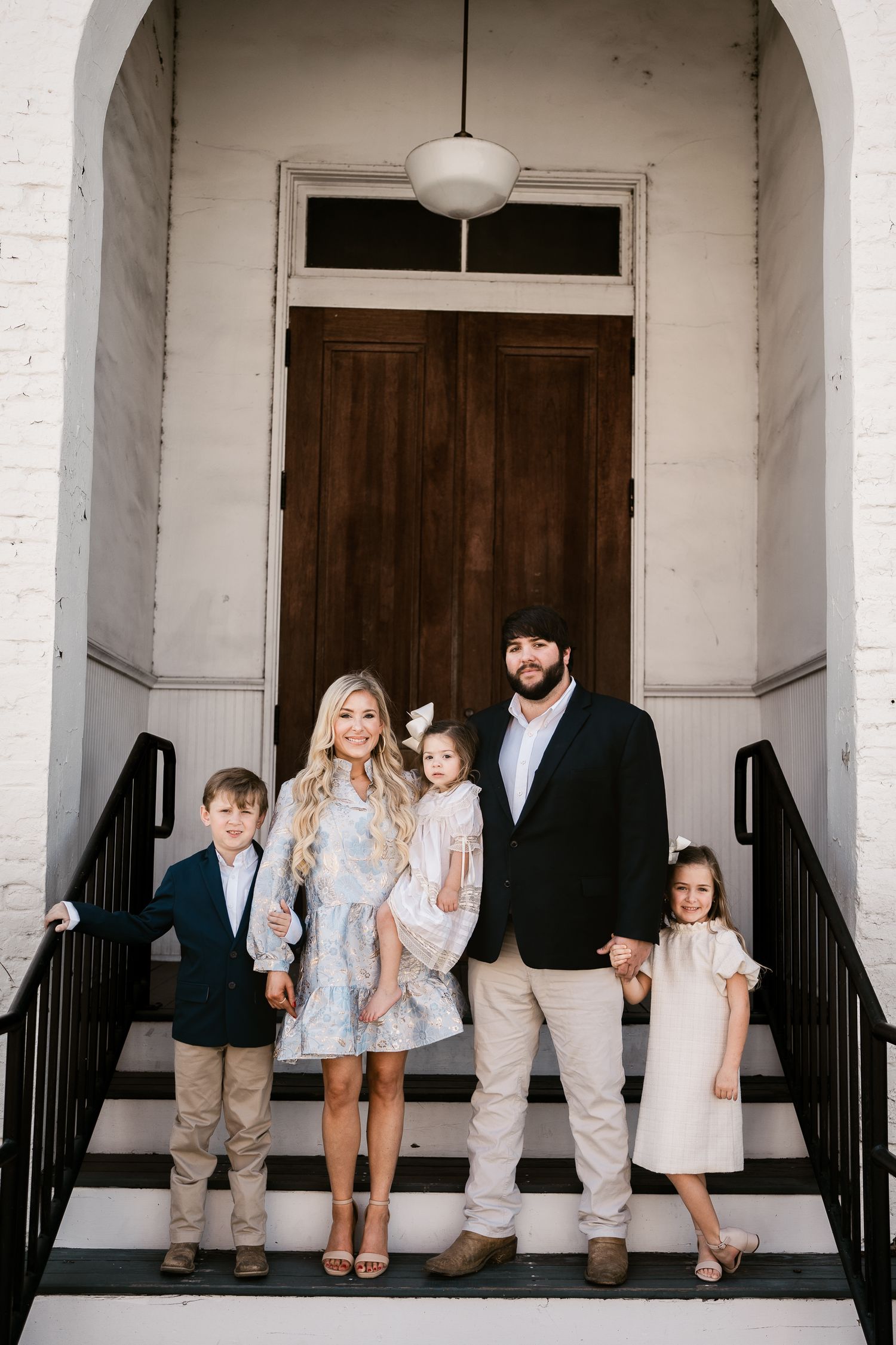 Family posed on white entrance steps with arched doorway wearing coordinated spring outfits.