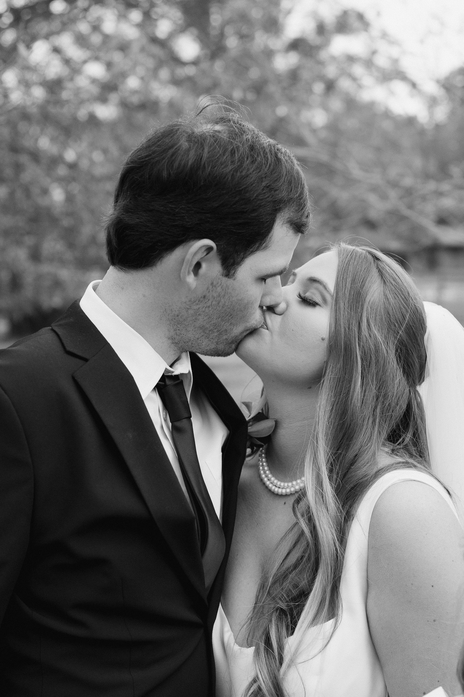 A romantic black and white wedding photo captures a couple sharing a tender kiss outdoors.