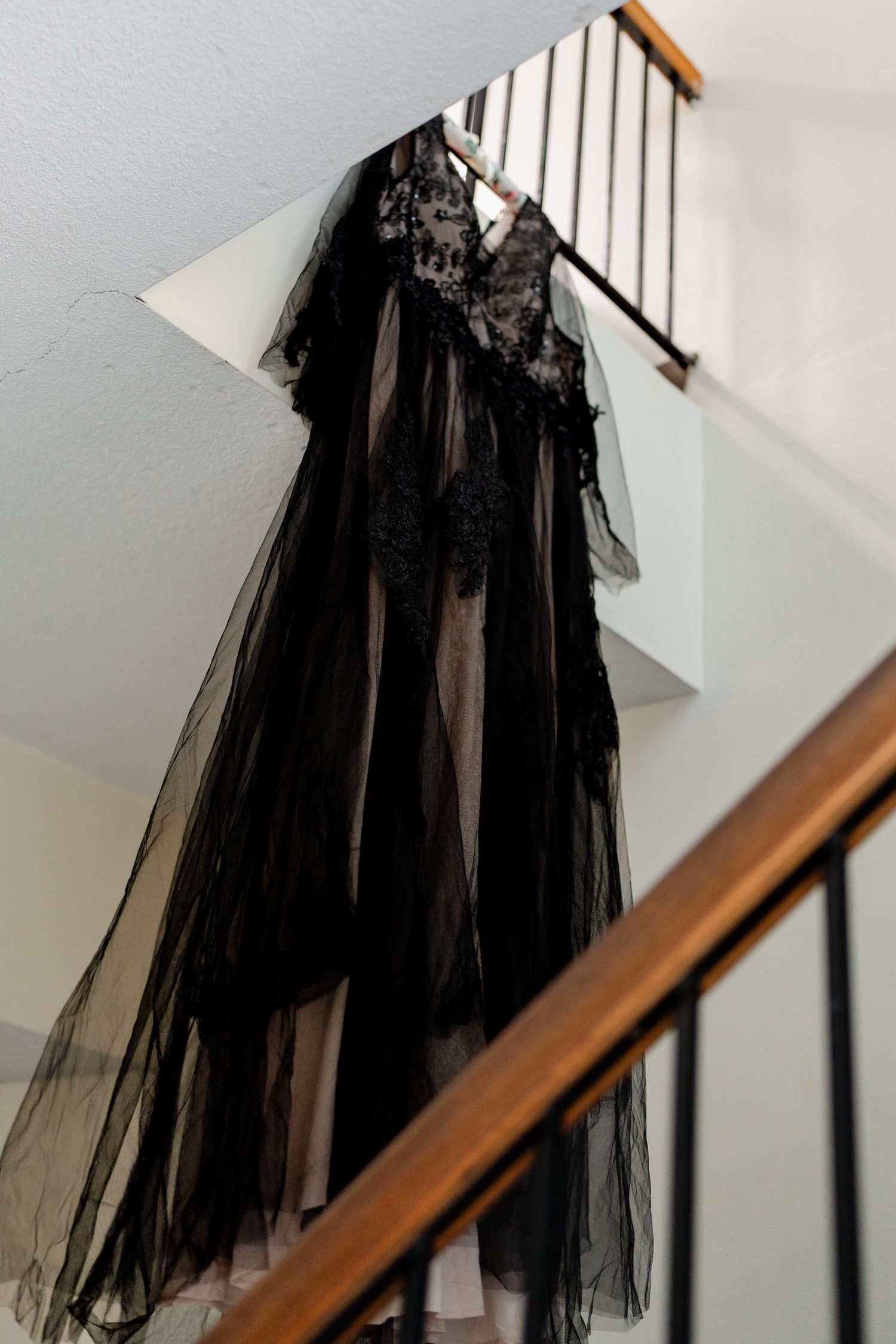 An elegant black lace and tulle evening gown with sheer overlay hangs on a staircase railing.