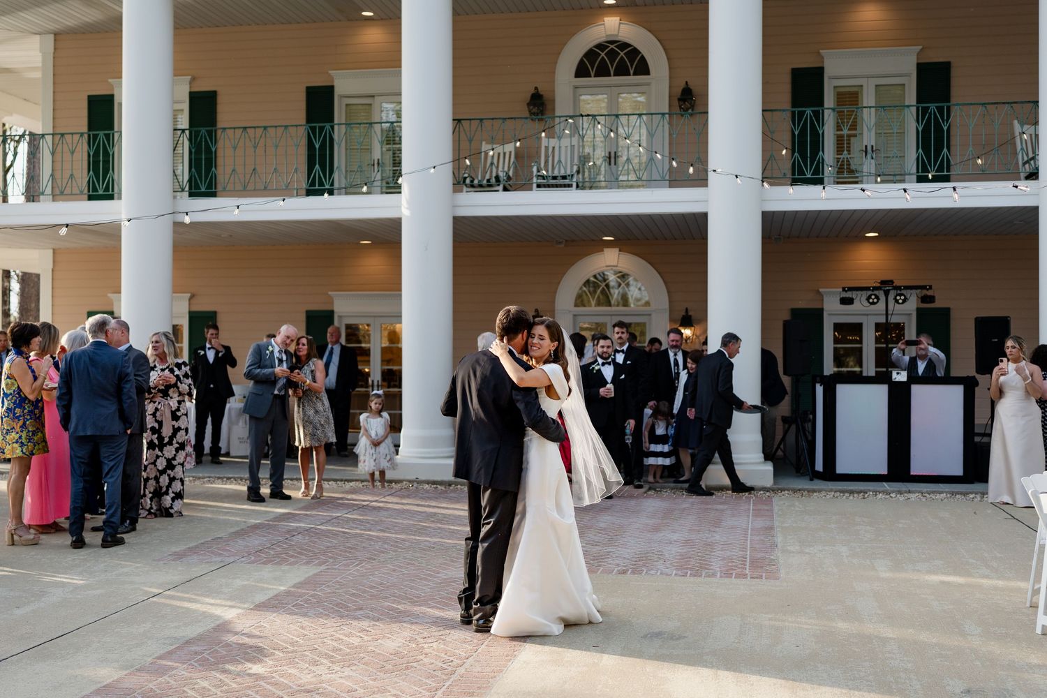 Wedding couple shares first dance surrounded by guests at elegant mansion venue.
