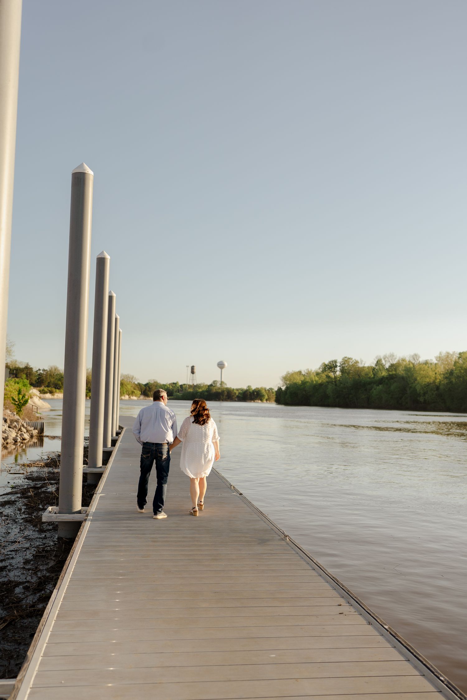Two figures walk together in silhouette along a wooden dock during sunset.