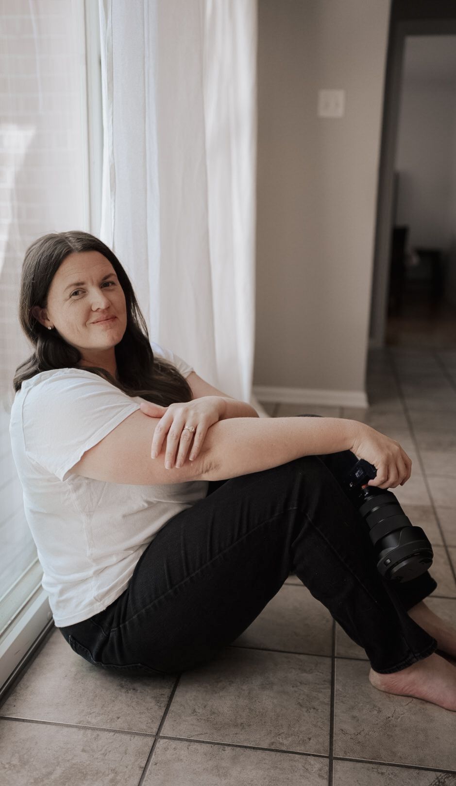A photographer sits casually by a window with camera equipment.