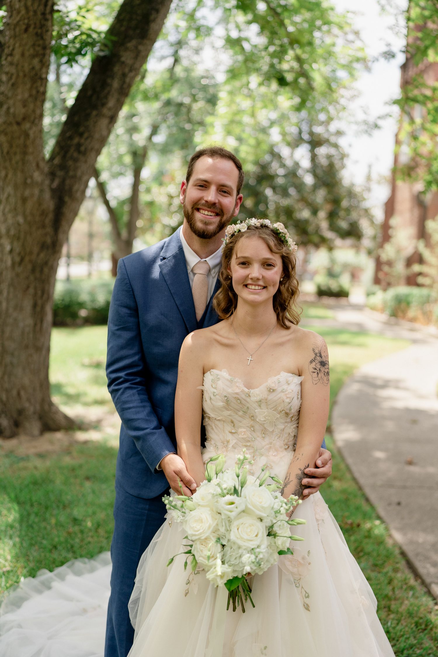 A joyful wedding couple shares candid moments together on a tree-lined path in a park setting.