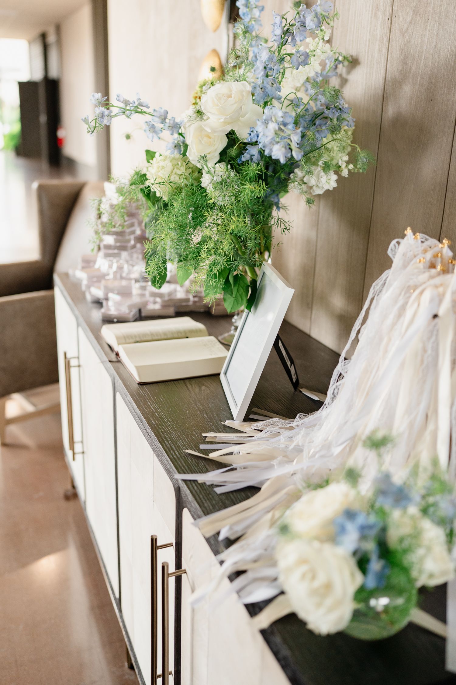 White floral arrangements with delicate blue accents decorate a rustic wooden surface in an elegant wedding setting.