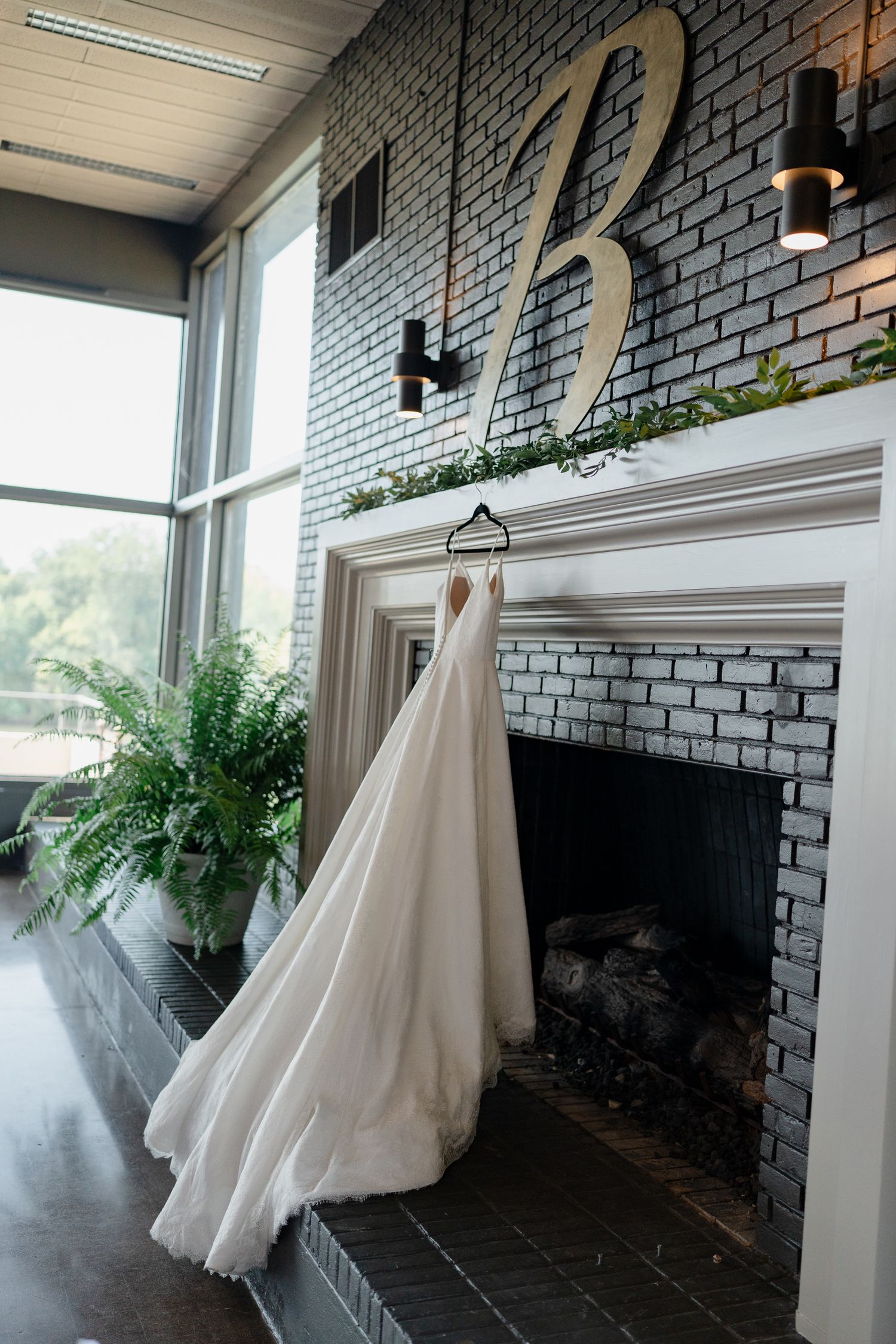 Wedding dresses hanging on display against a grey brick wall with ferns and natural lighting.