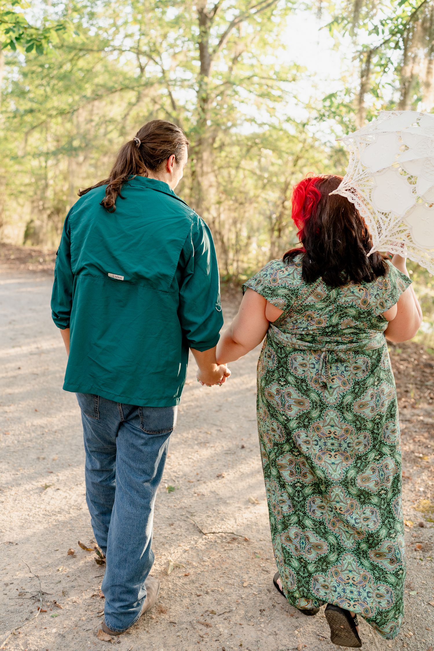 Two people walk hand in hand down a wooded path wearing casual clothes in matching teal and floral prints.