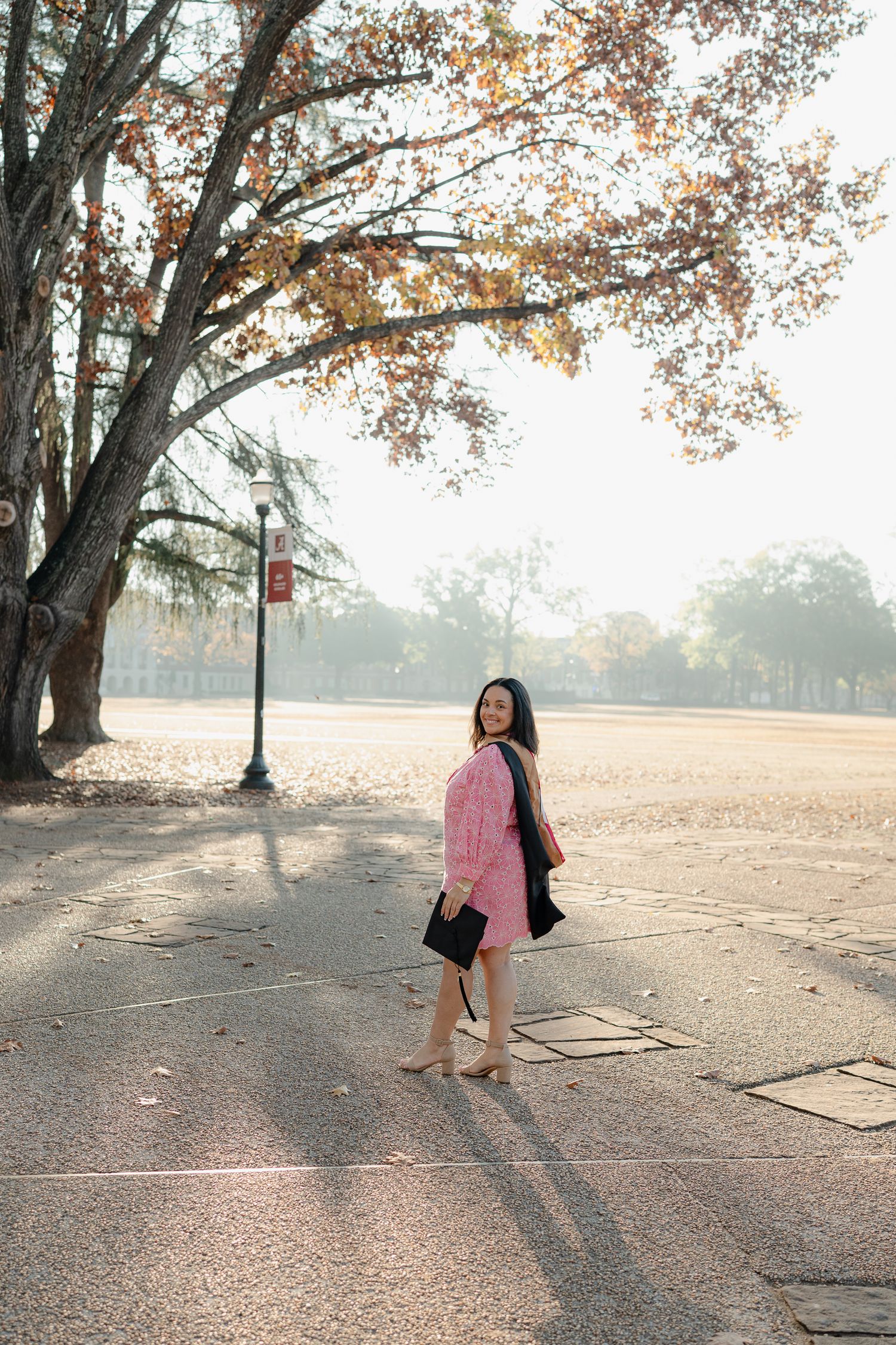 Autumn graduation photoshoot with sunlit trees and long shadows on campus grounds.