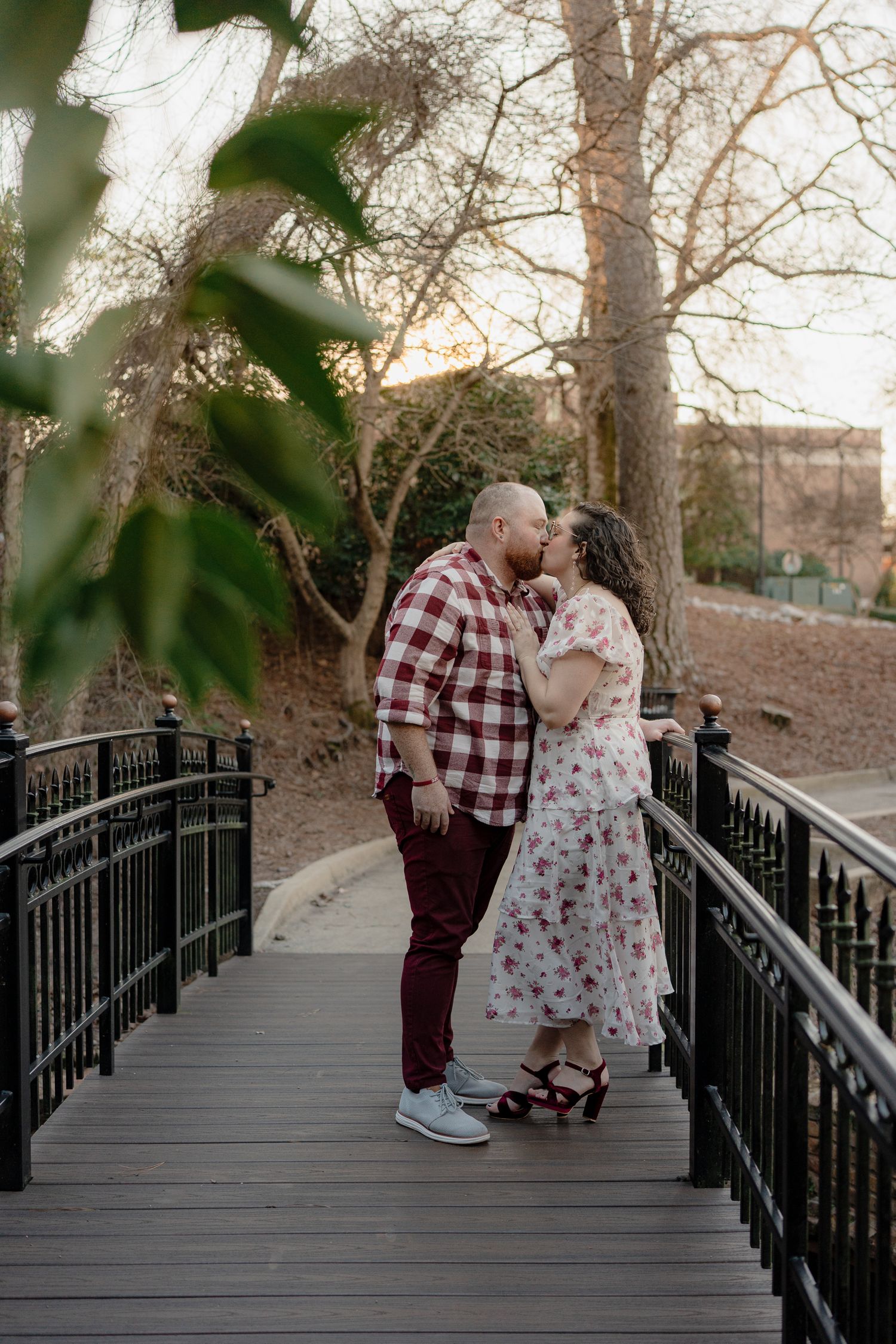 Romantic couple embraces on wooden bridge pathway surrounded by trees at dusk.