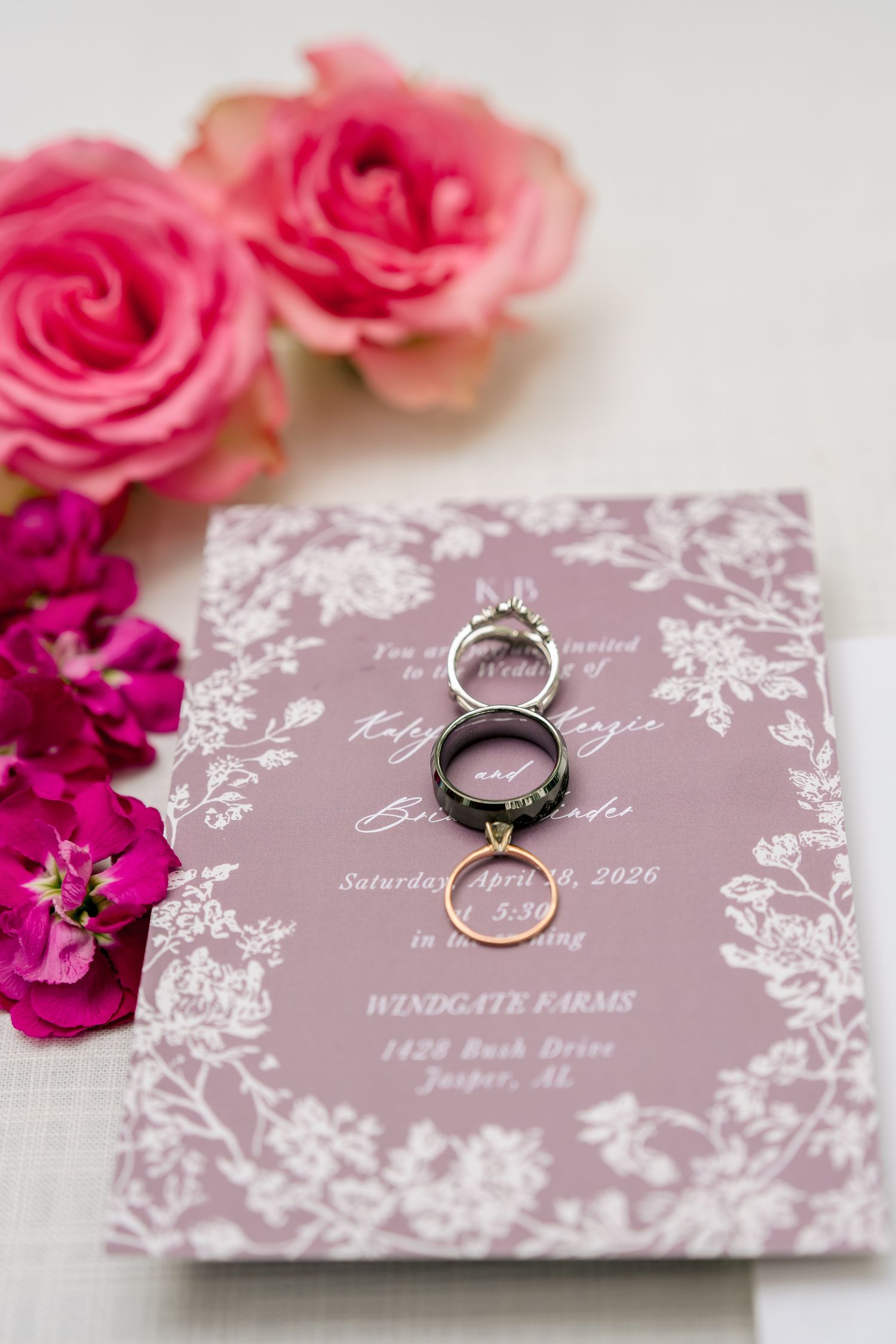Pink floral wedding invitation with diamond engagement ring and gold wedding bands at Windgate Farms in Jasper AL.