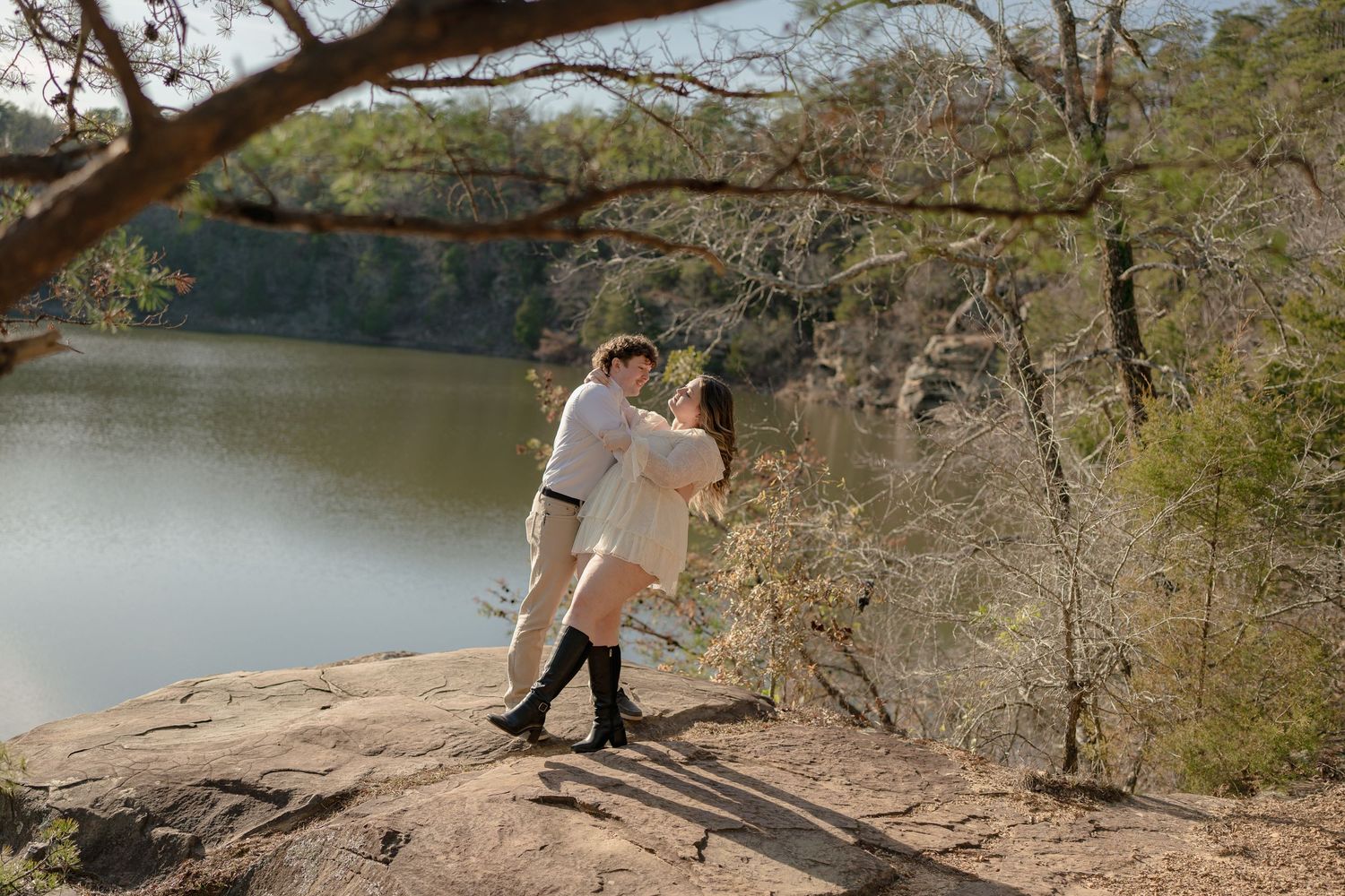 Couple embracing on a rocky overlook above a serene lake surrounded by autumn trees.