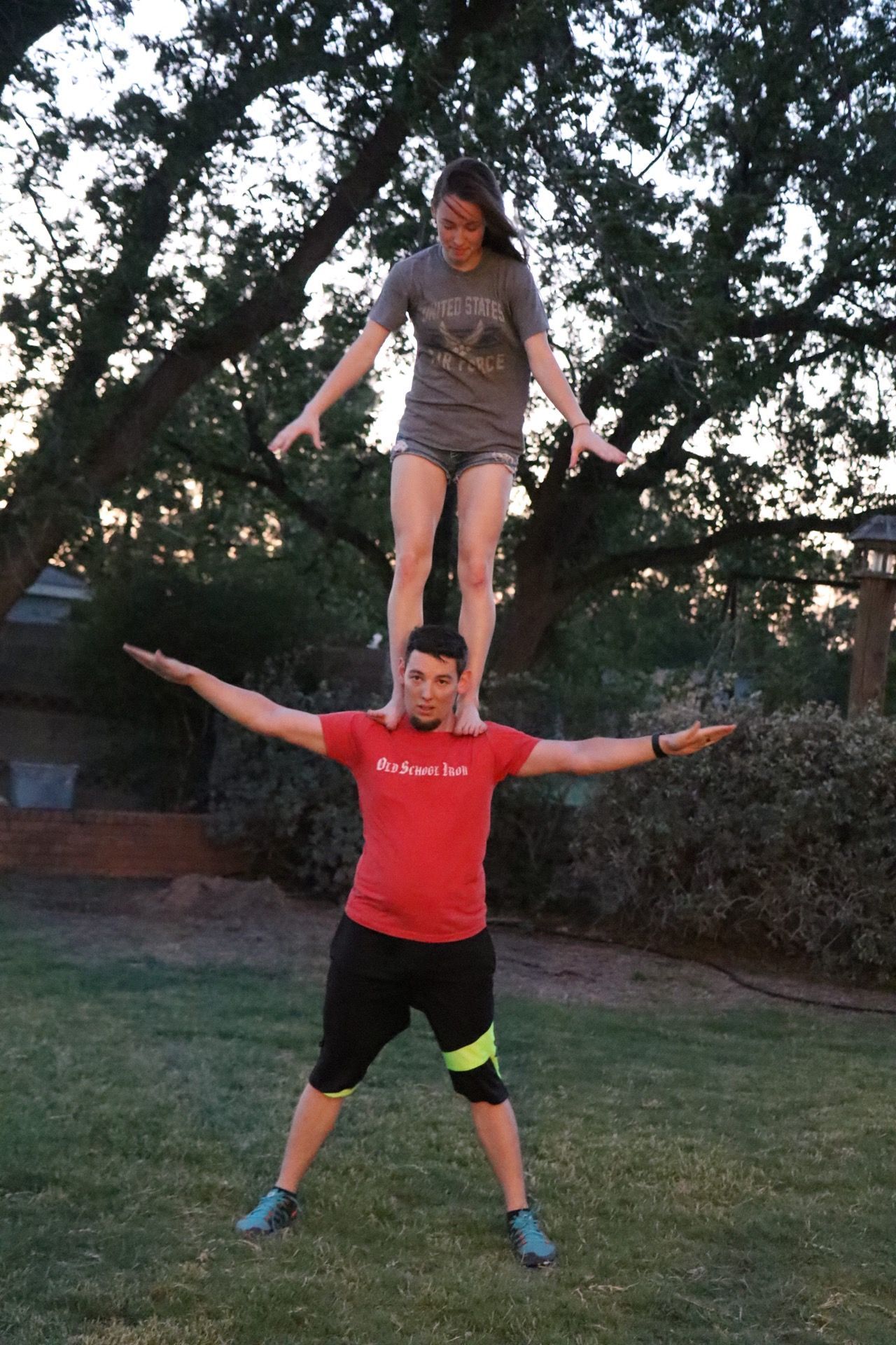 People jumping and playing in a backyard at sunset with trees in the background.