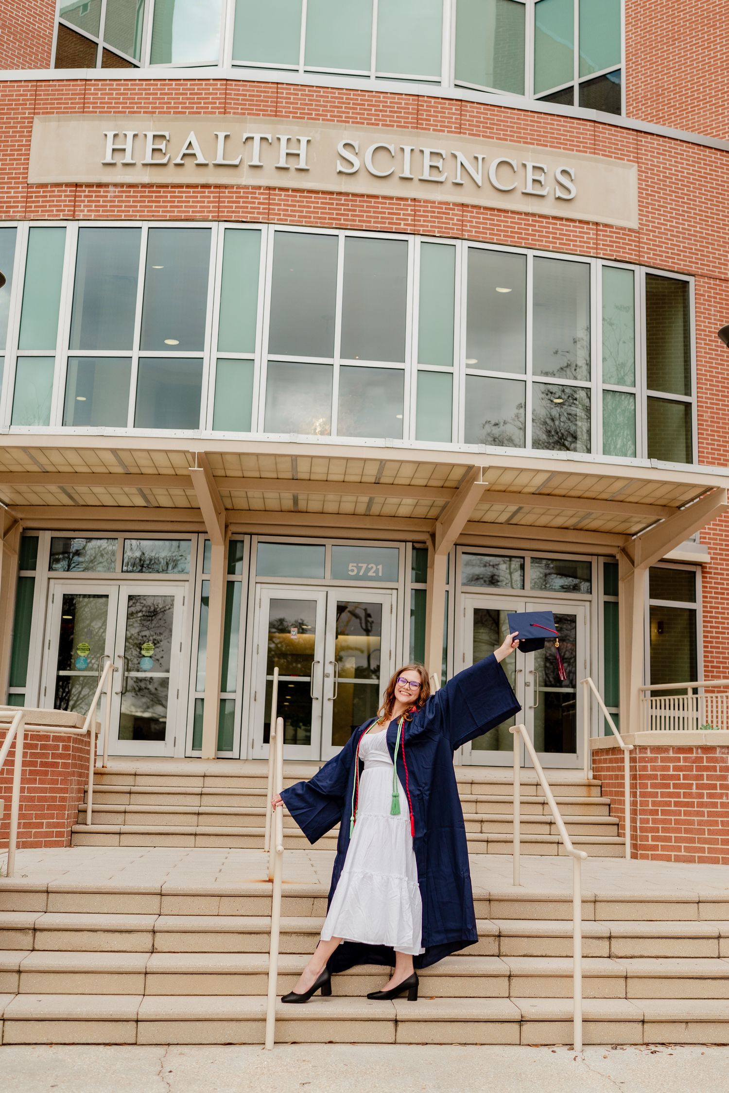 Steps of Health Sciences building with white columns frame celebratory graduation poses.