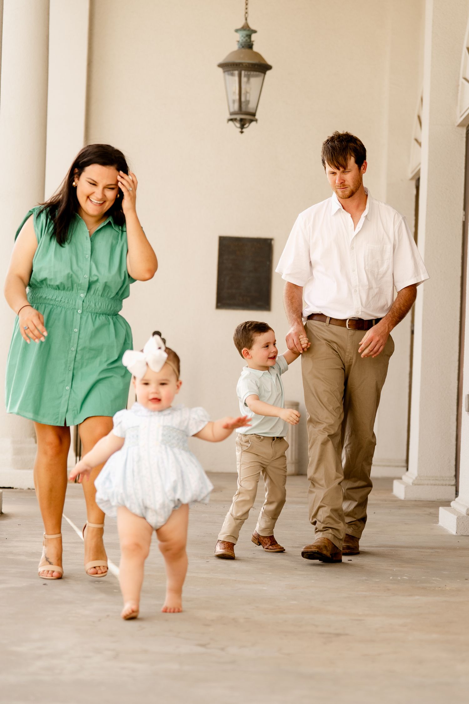 Family in casual attire walking and playing together on columned porch.