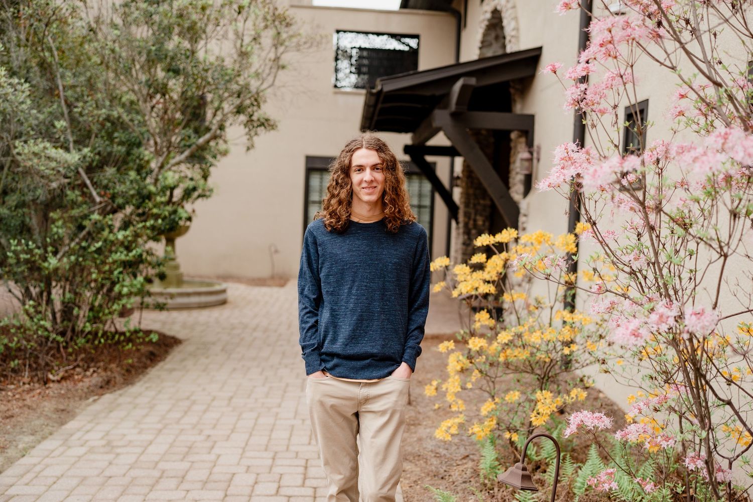 Person in navy sweater posing on brick pathway with yellow and pink flowers in garden.